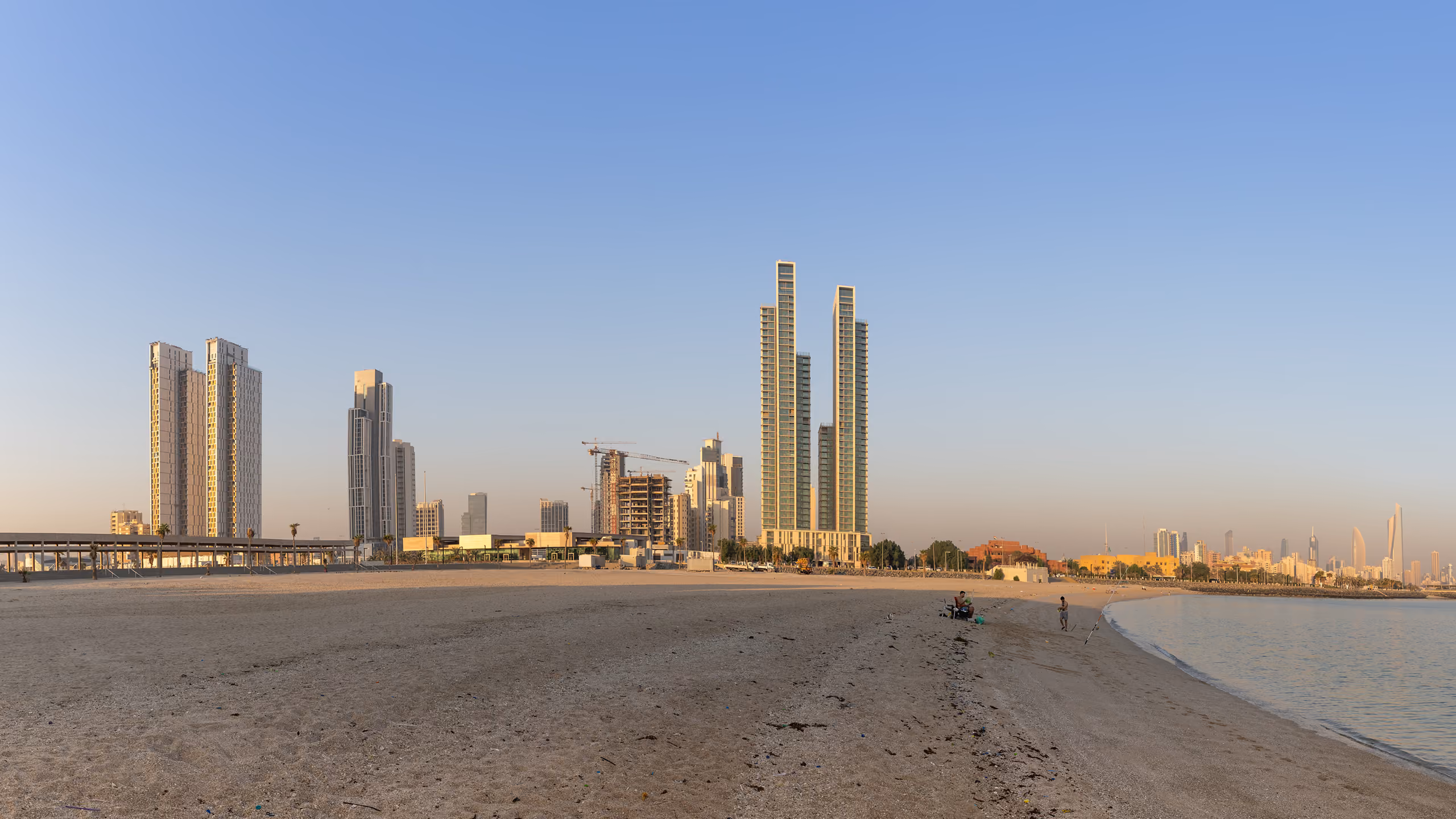 Twin slender towers of Hessah Al Mubarak rising above the Kuwait City skyline, seen from a beach along the waterfront