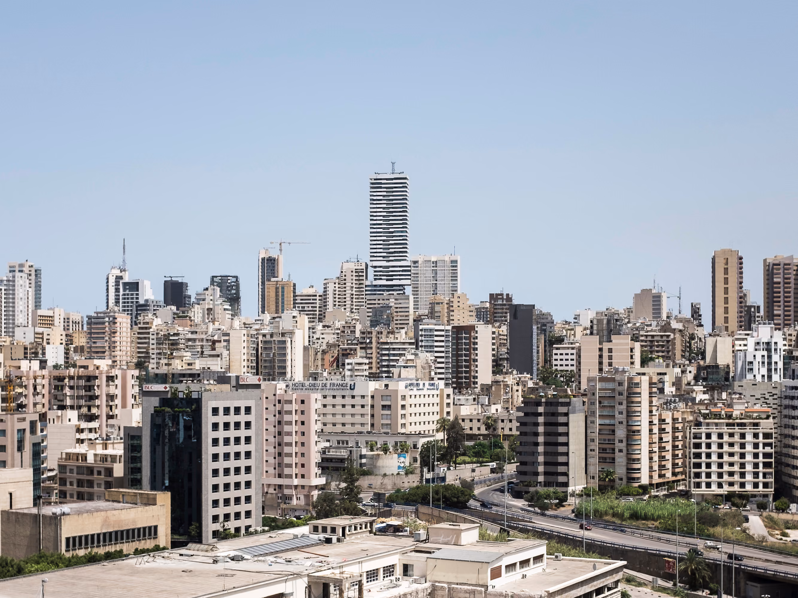 Skygate tower rising above the dense Beirut skyline, its striped facade distinct among surrounding mid-rise buildings and the coastal highway below