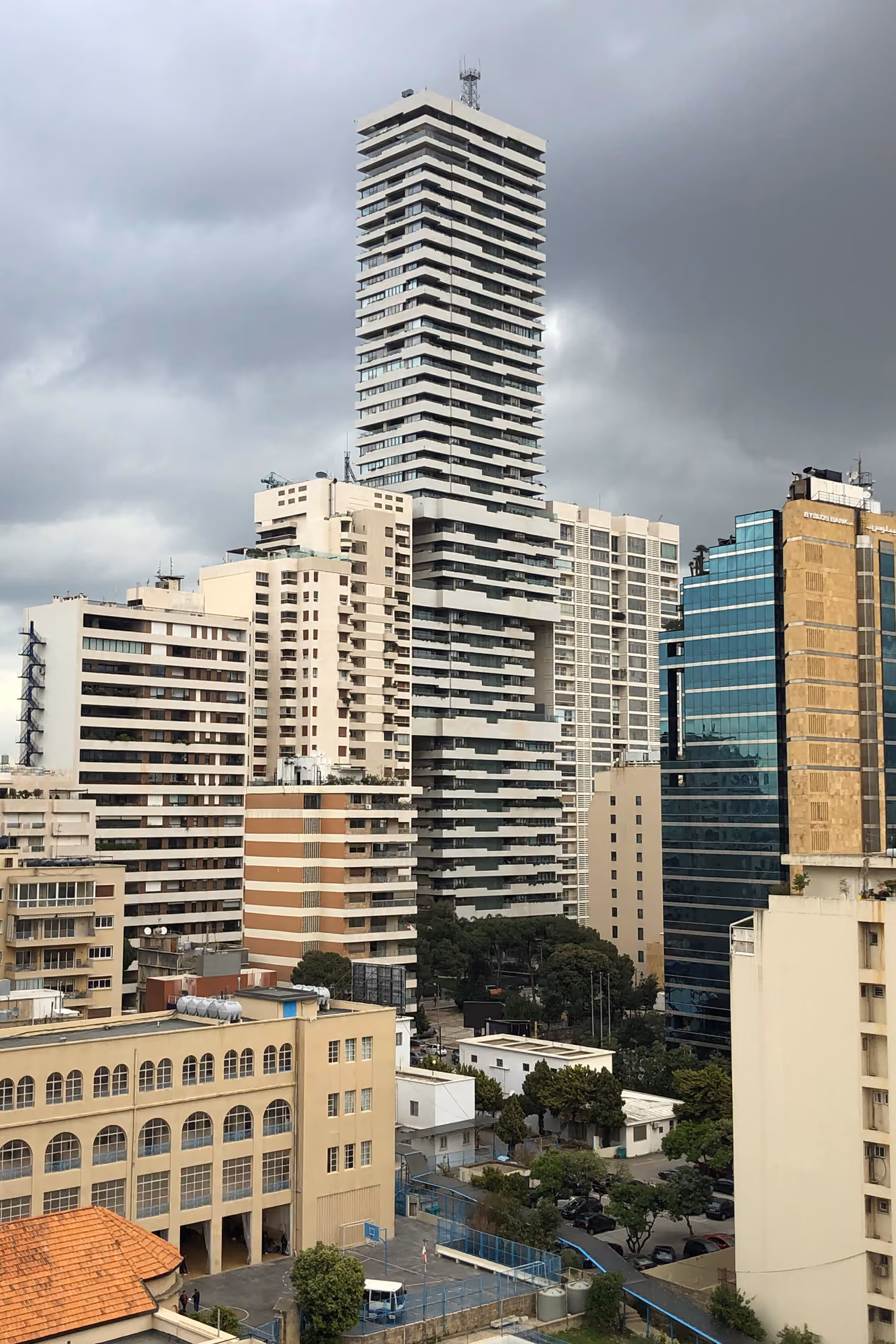 Skygate tower rising above Beirut's Ashrafieh skyline, its stacked white volumes with cantilevered edges standing out among surrounding mid-rise buildings under a cloudy sky