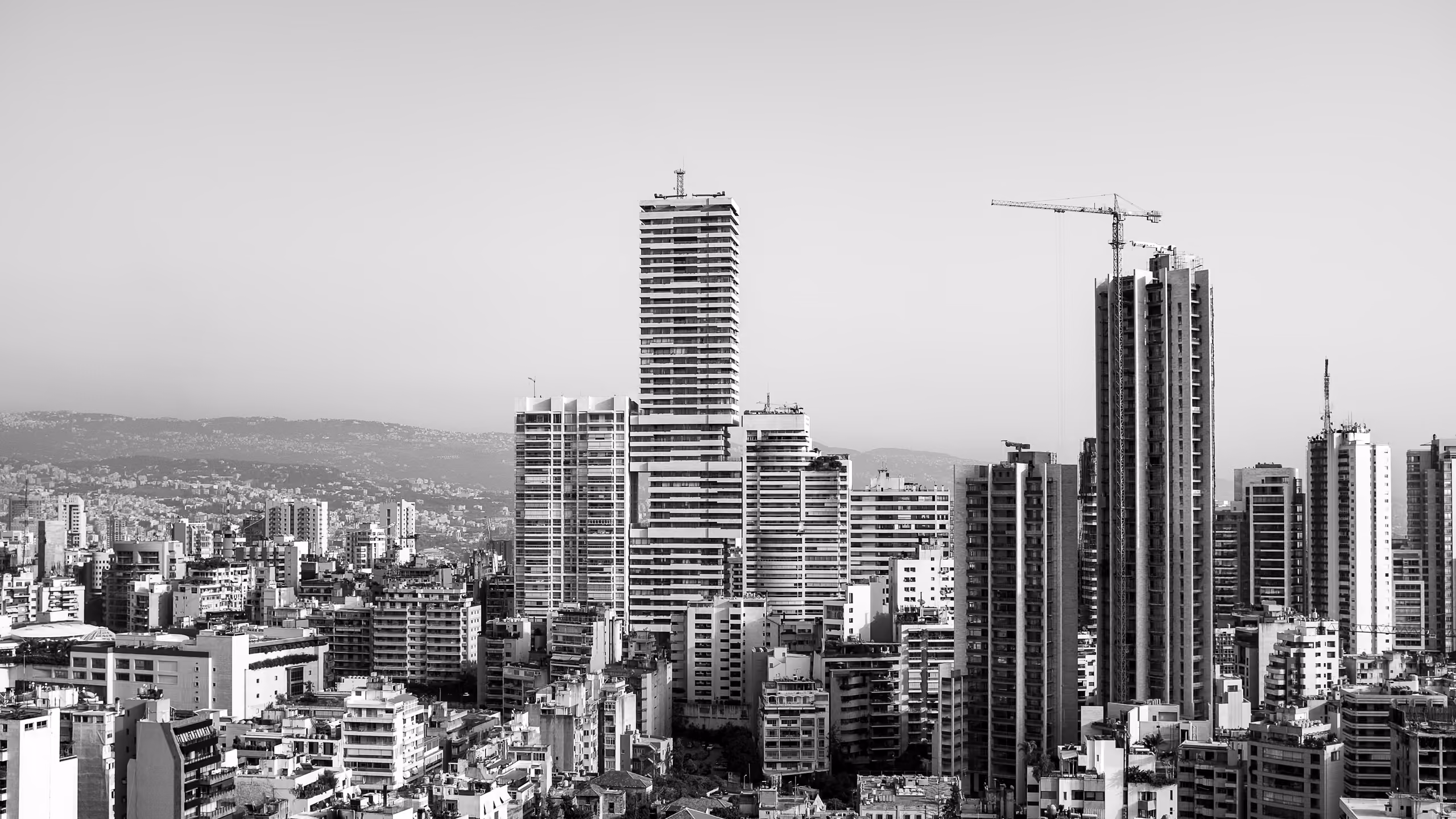 Black and white skyline view of Beirut with Skygate's stacked cubic tower rising above dense mid-rise buildings, a construction crane visible nearby