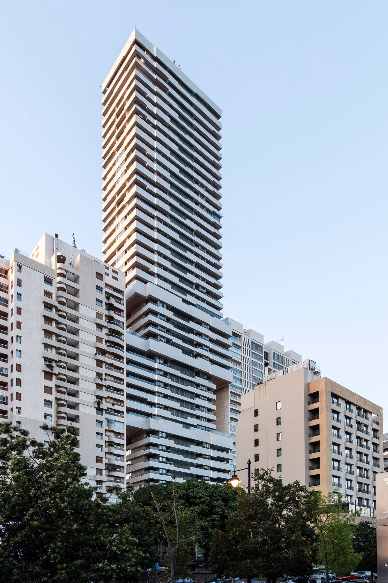 Skygate tower rising above surrounding Beirut buildings, its stacked cubical volumes creating staggered cantilevered terraces against a clear sky