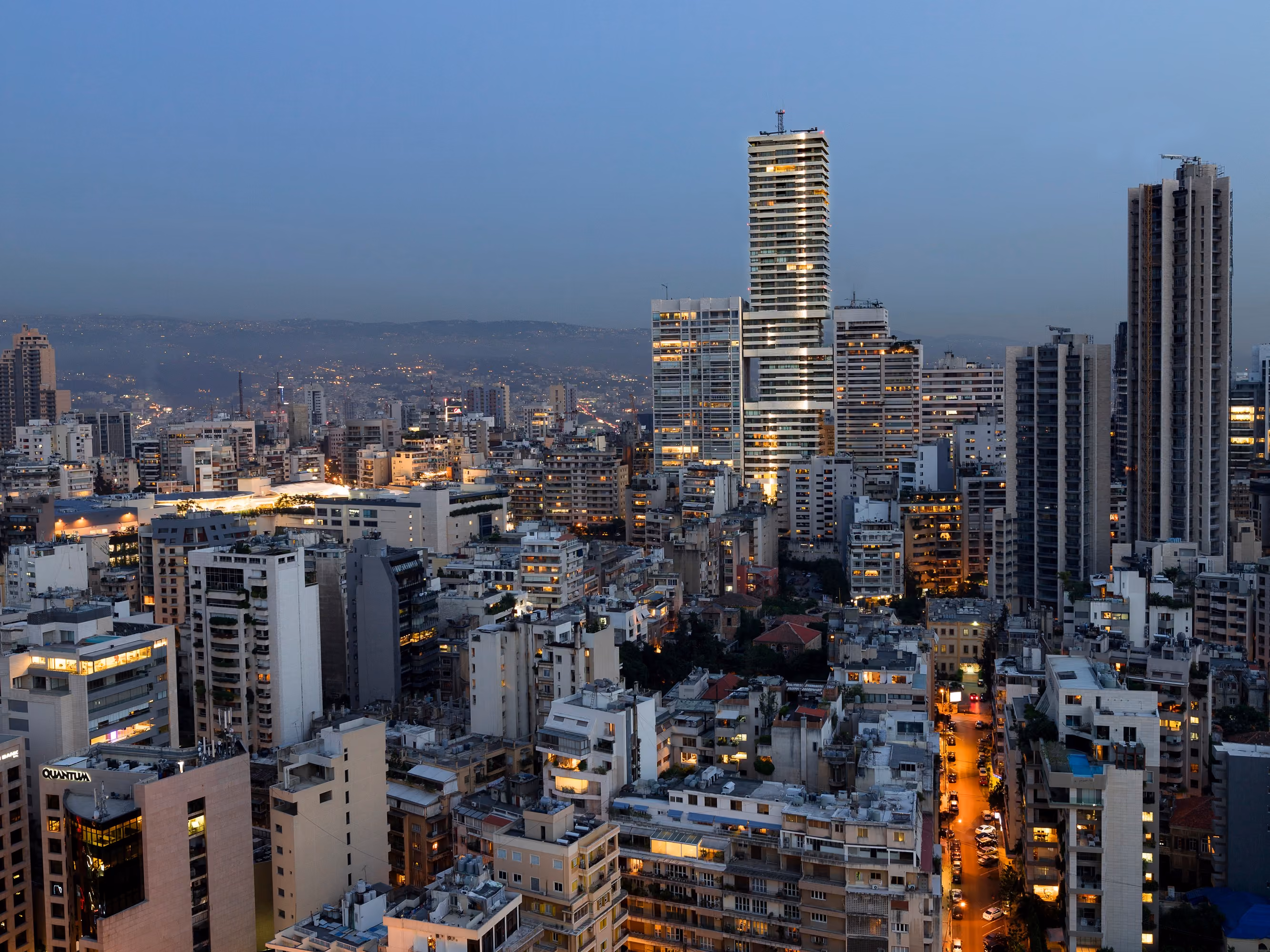 Skygate tower illuminated at dusk, rising above the dense rooftops of Beirut with the city and hills fading into evening haze