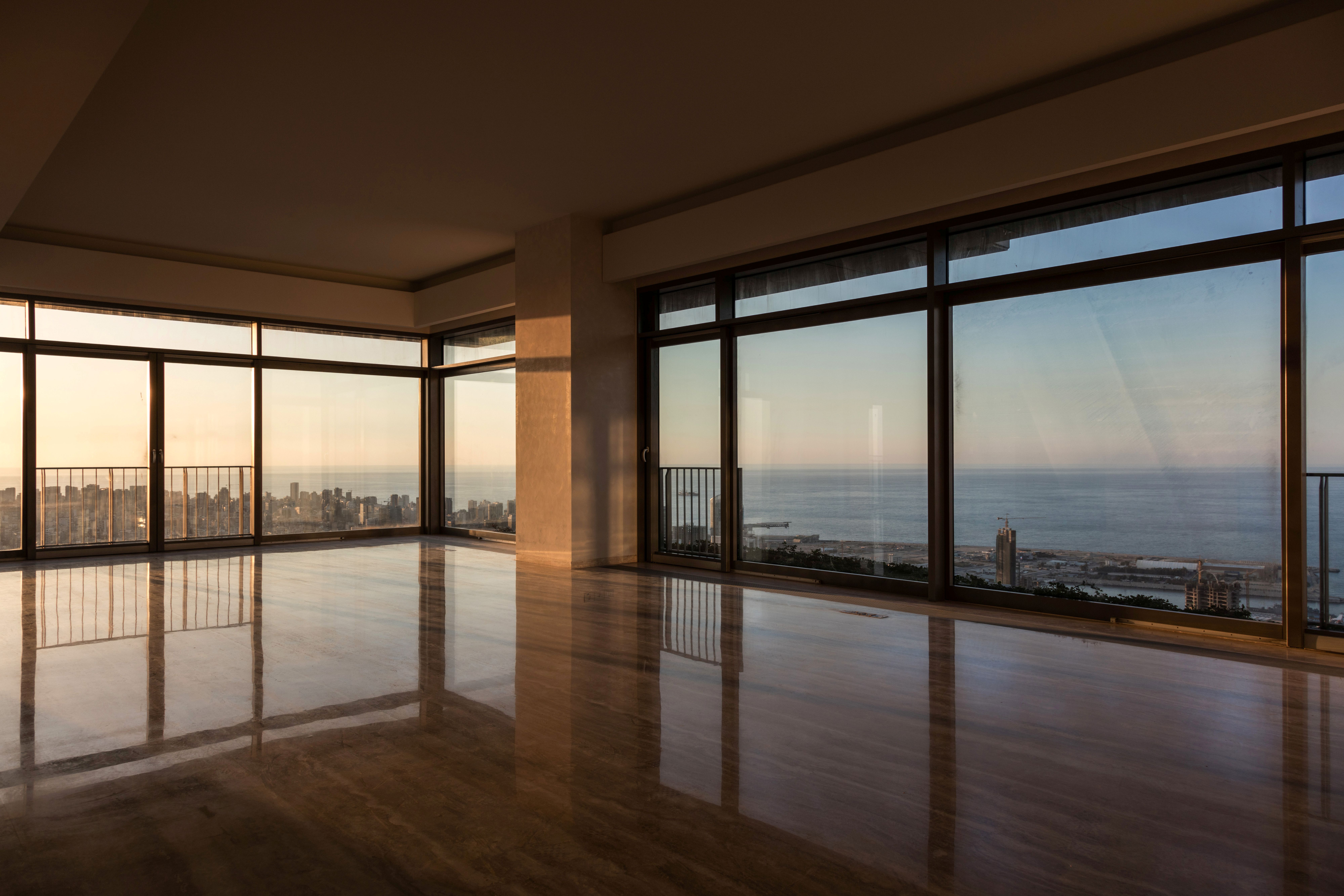 Empty corner unit in Skygate, Beirut, floor-to-ceiling windows framing the coastline and city skyline at sunset over polished marble floors
