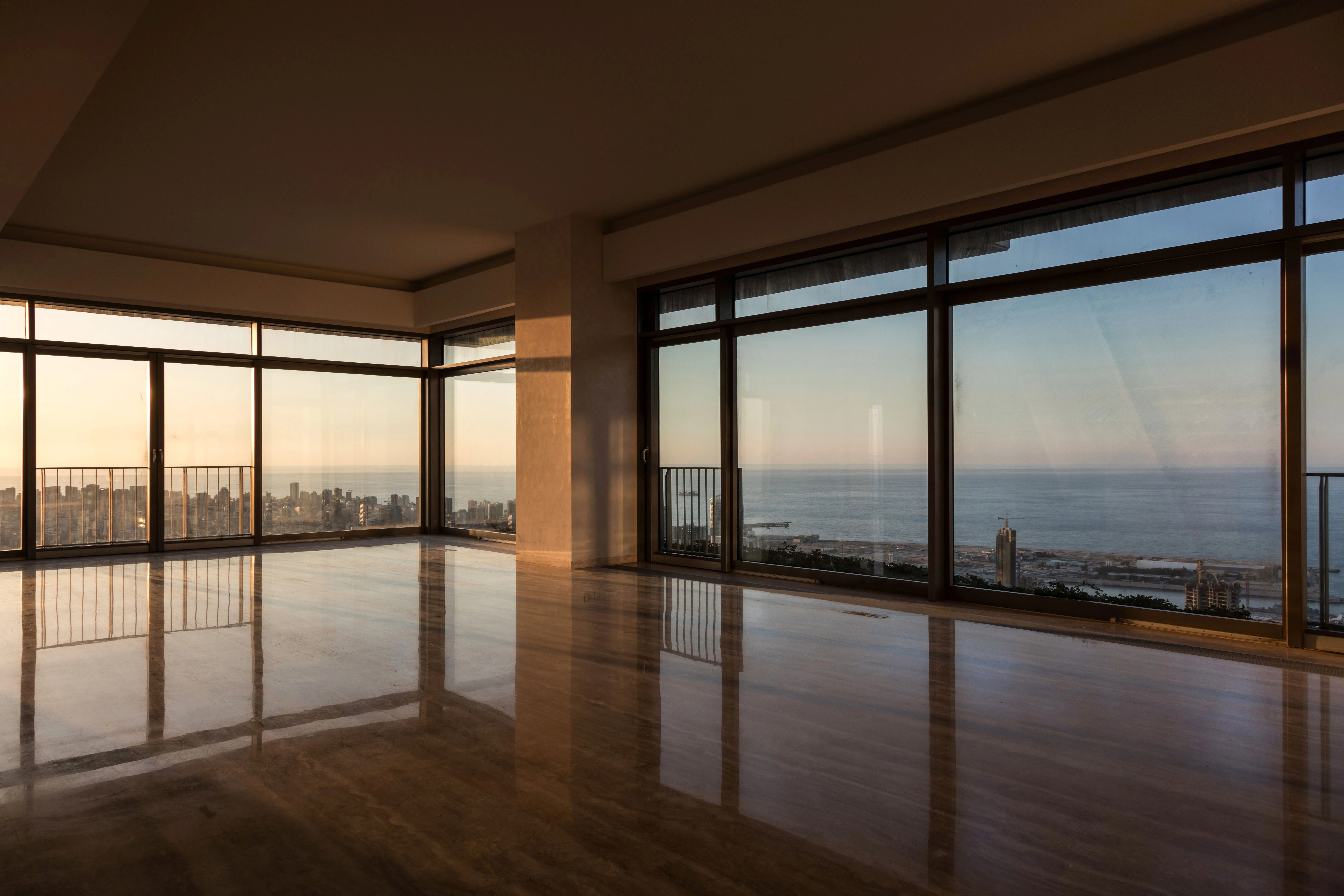 Empty corner unit in Skygate, Beirut, floor-to-ceiling windows framing the coastline and city skyline at sunset over polished marble floors