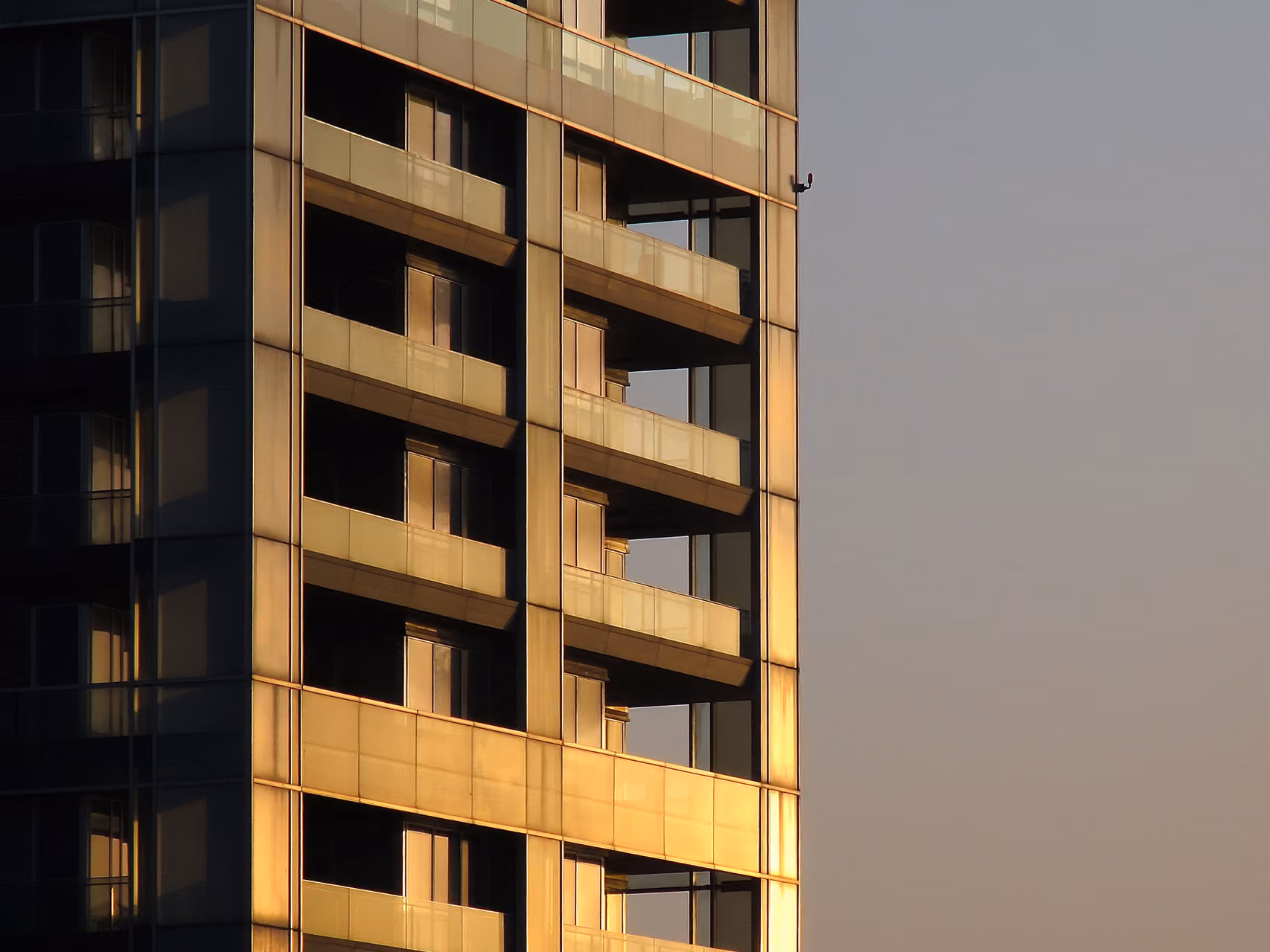 Corner facade of Platinum Tower in Beirut at sunset, stacked glass-cornered balconies glowing amber against a hazy sky