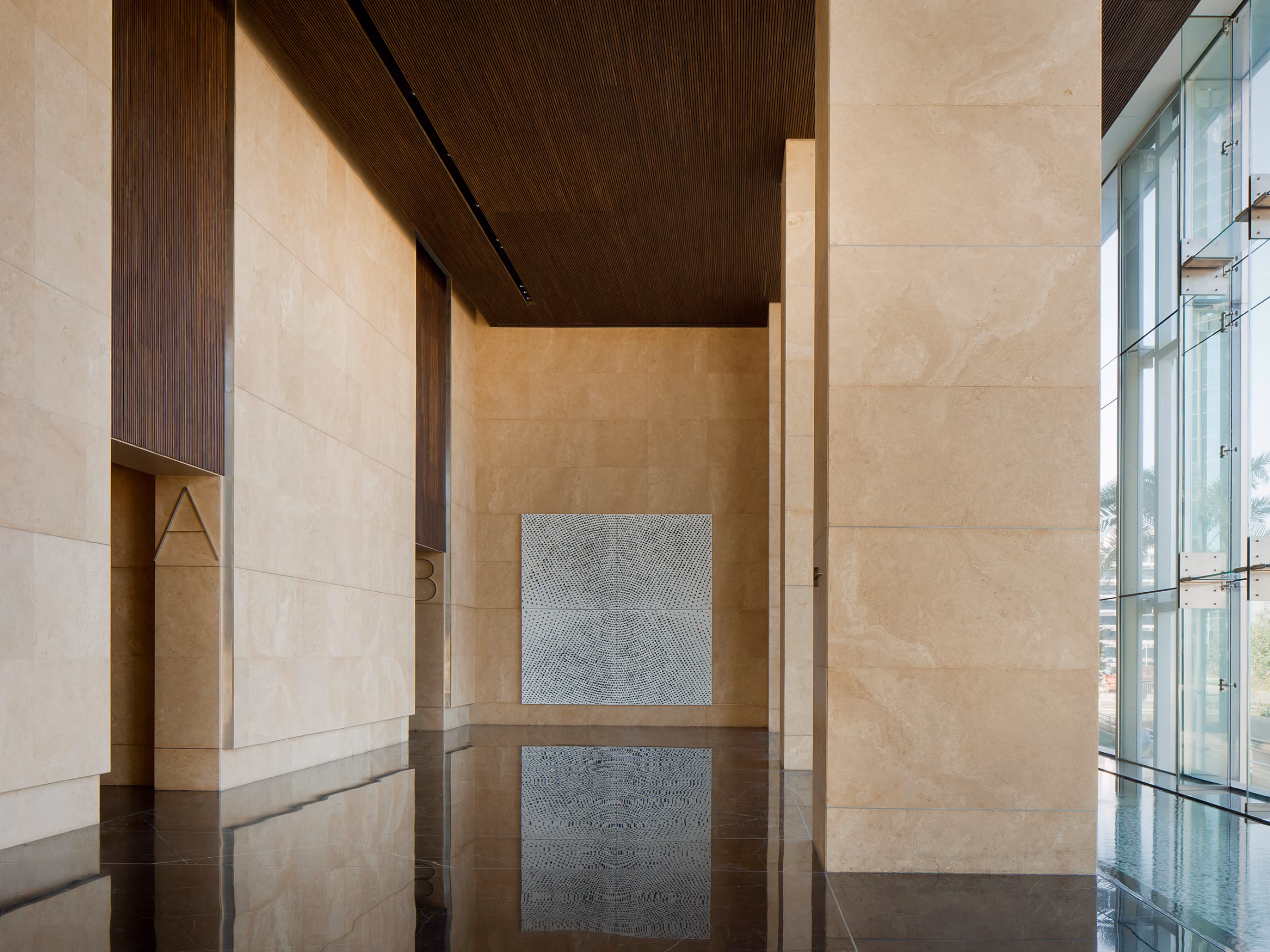 Lobby of Platinum Tower in Beirut, polished stone walls and dark ceiling framing a textured art panel, reflected in the glossy black floor
