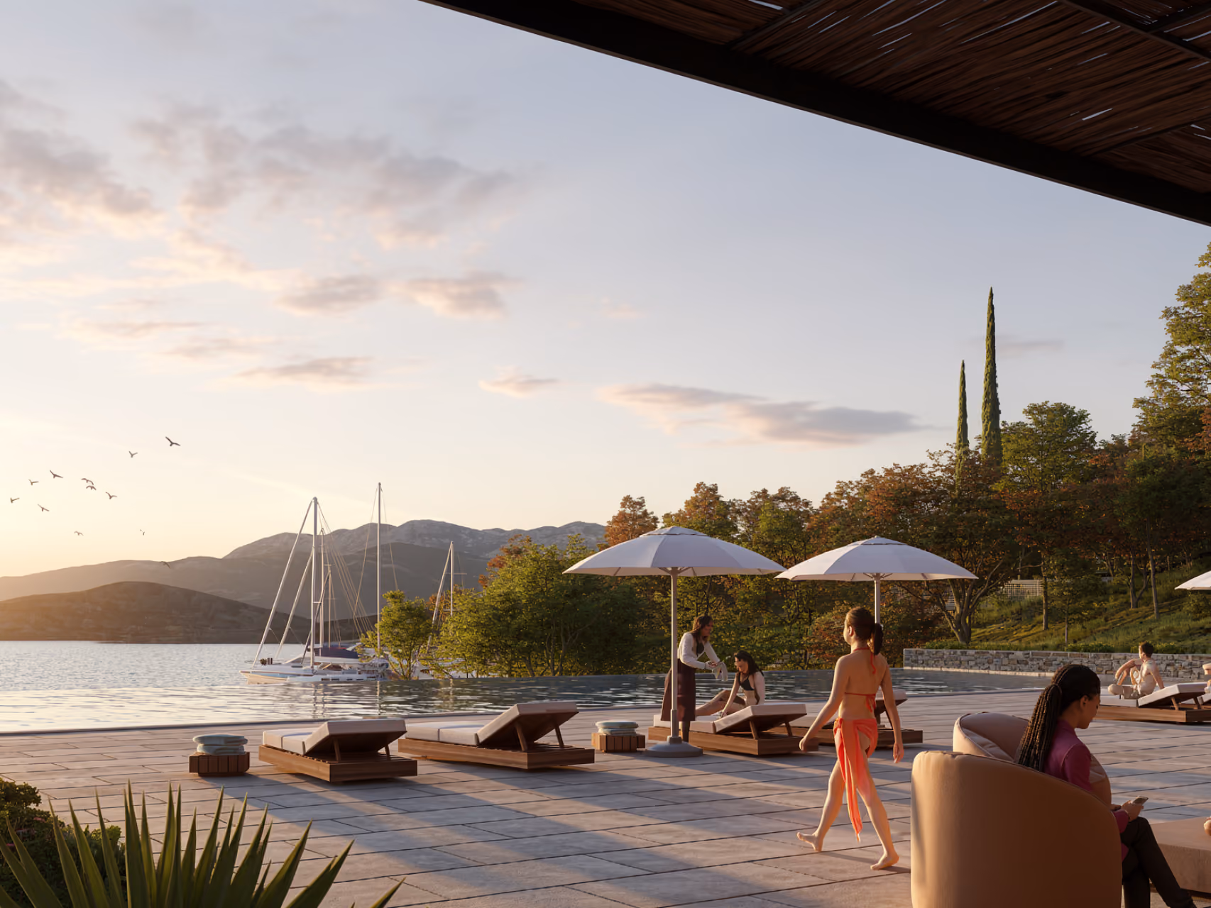 Poolside terrace at Tivat Hotel and Beach Resort in Tivat, loungers and umbrellas overlooking a bay with sailboats at sunset