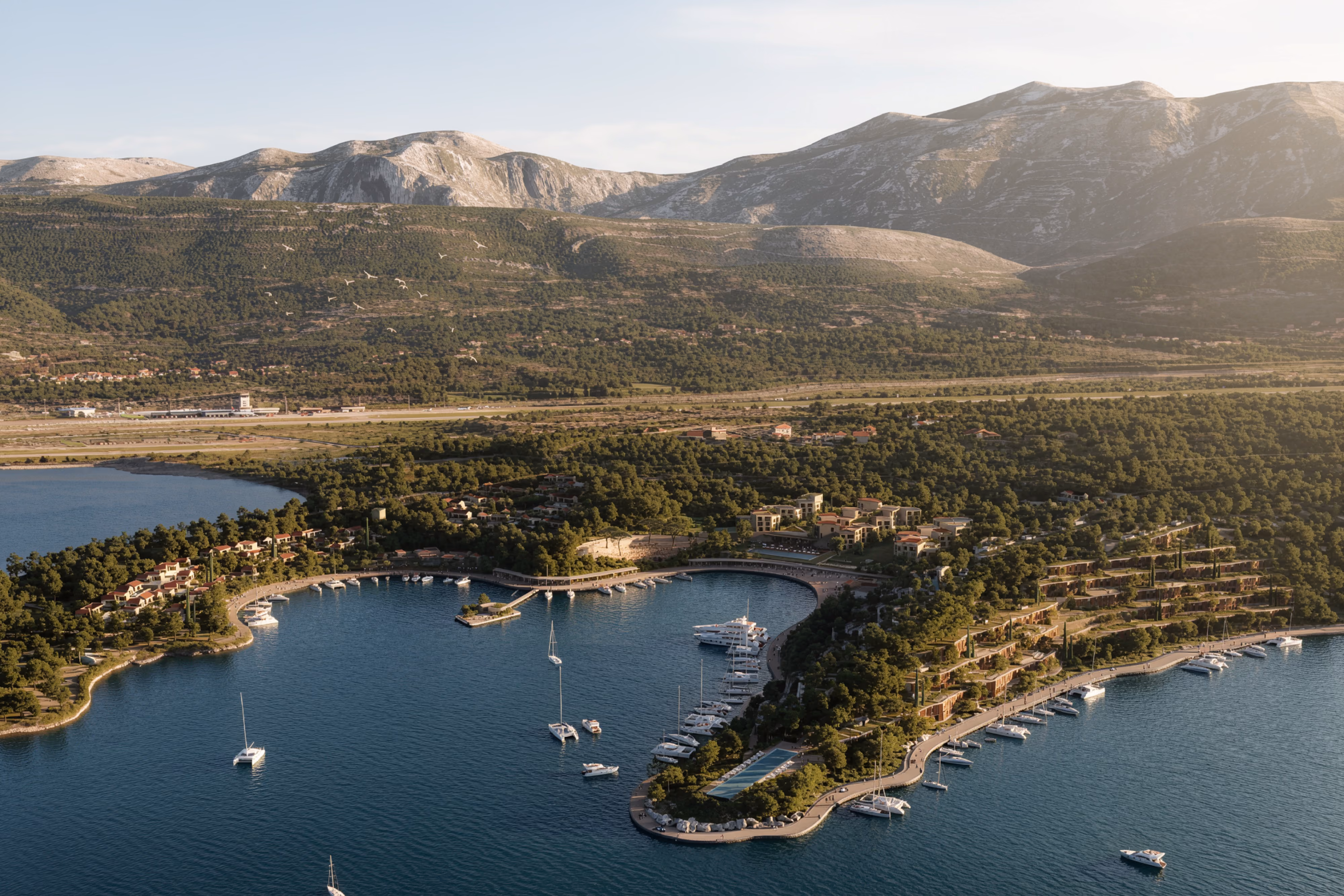 Tivat Hotel and Beach Resort in Tivat, Montenegro, aerial view of a curved marina lined with low-rise buildings and villas amid forested hills