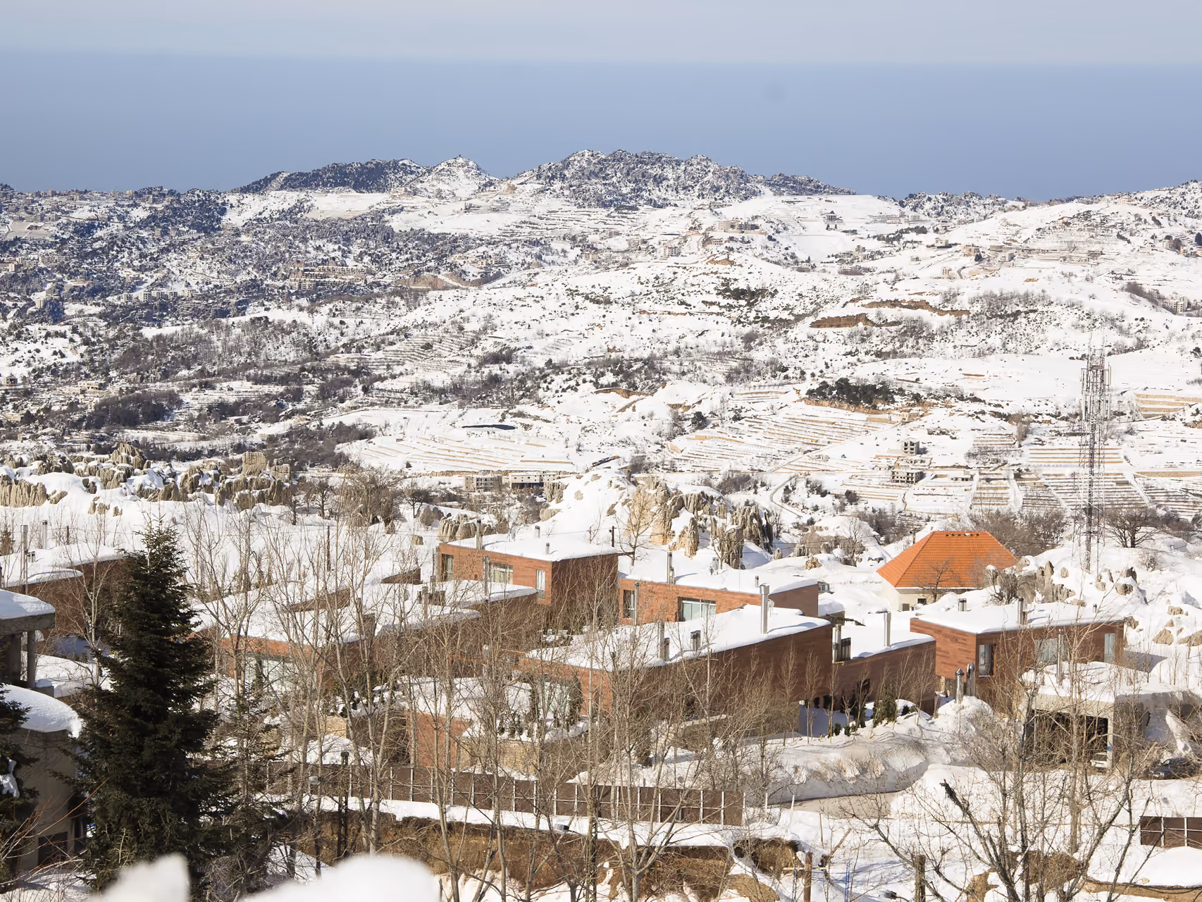 Snow-covered mountain landscape of Clouds villas in Faqra, wooden volumes with terraced roofs nestled among rocky outcrops and pine trees