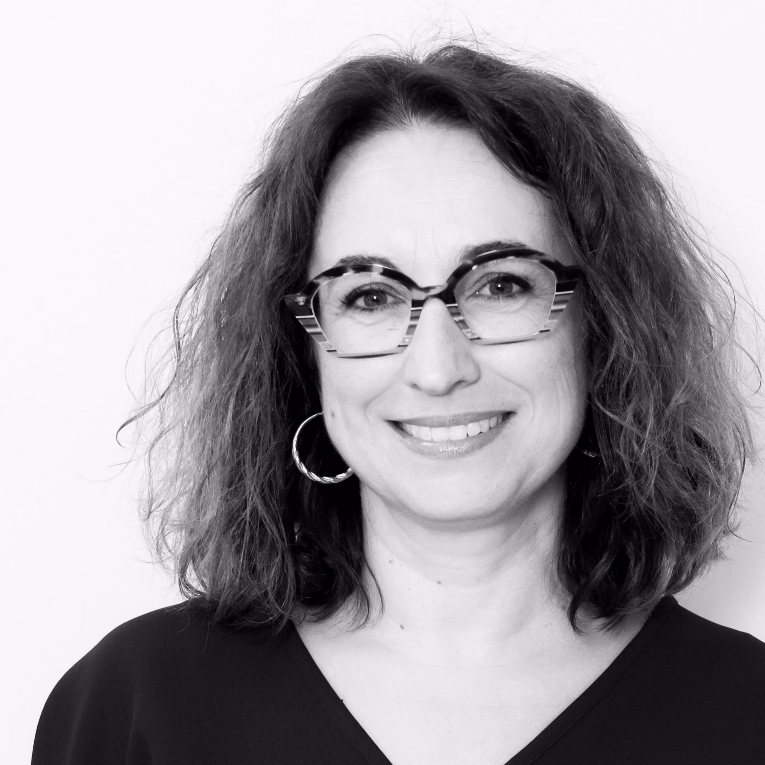 Carme Raventos, Senior Executive Assistant at Nabil Gholam Architects, black and white portrait smiling in glasses with wavy shoulder-length hair