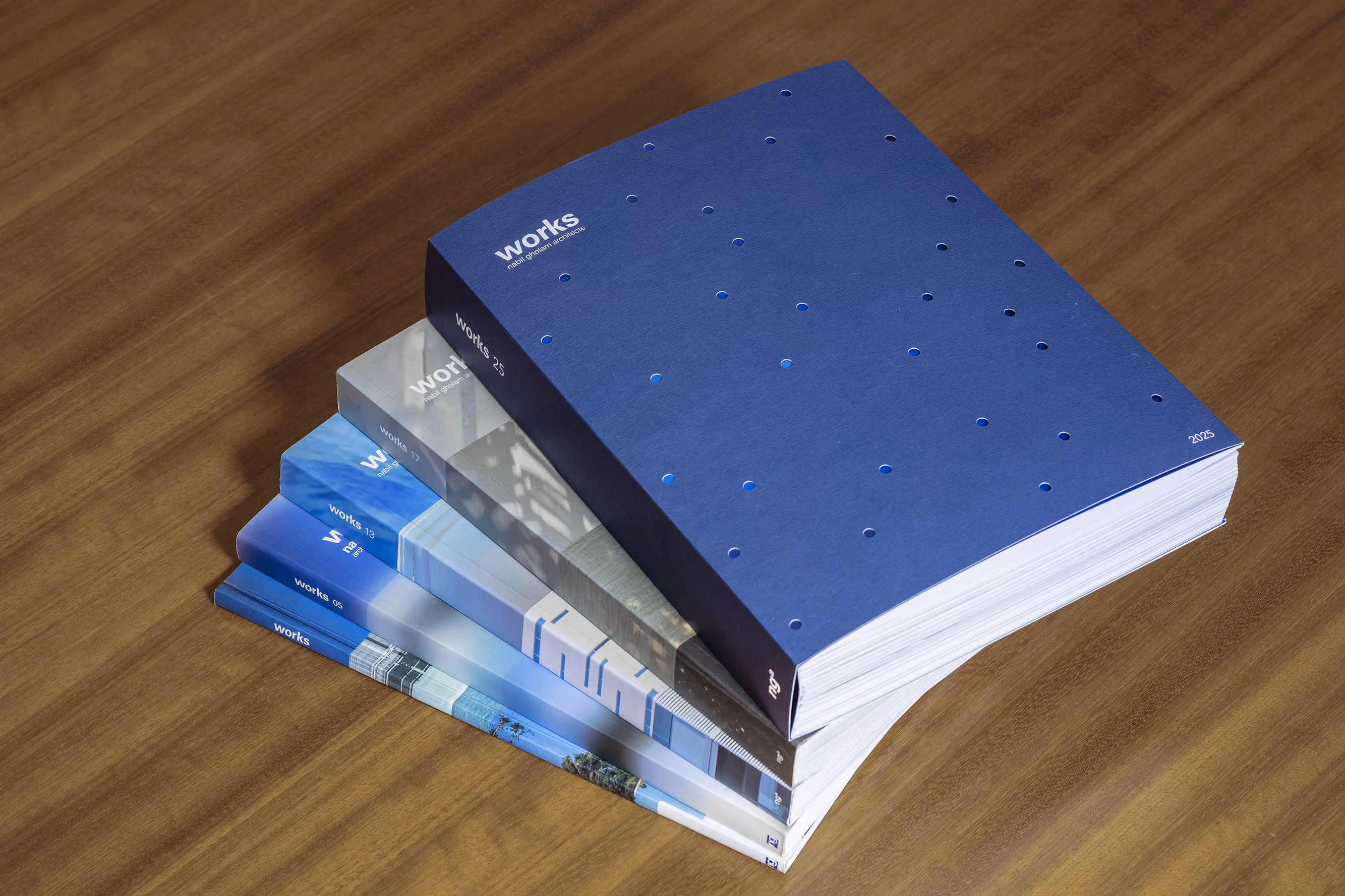 Stacked editions of Works, Nabil Gholam Architects' project monograph series, with the blue perforated-cover 2025 volume on top of earlier issues
