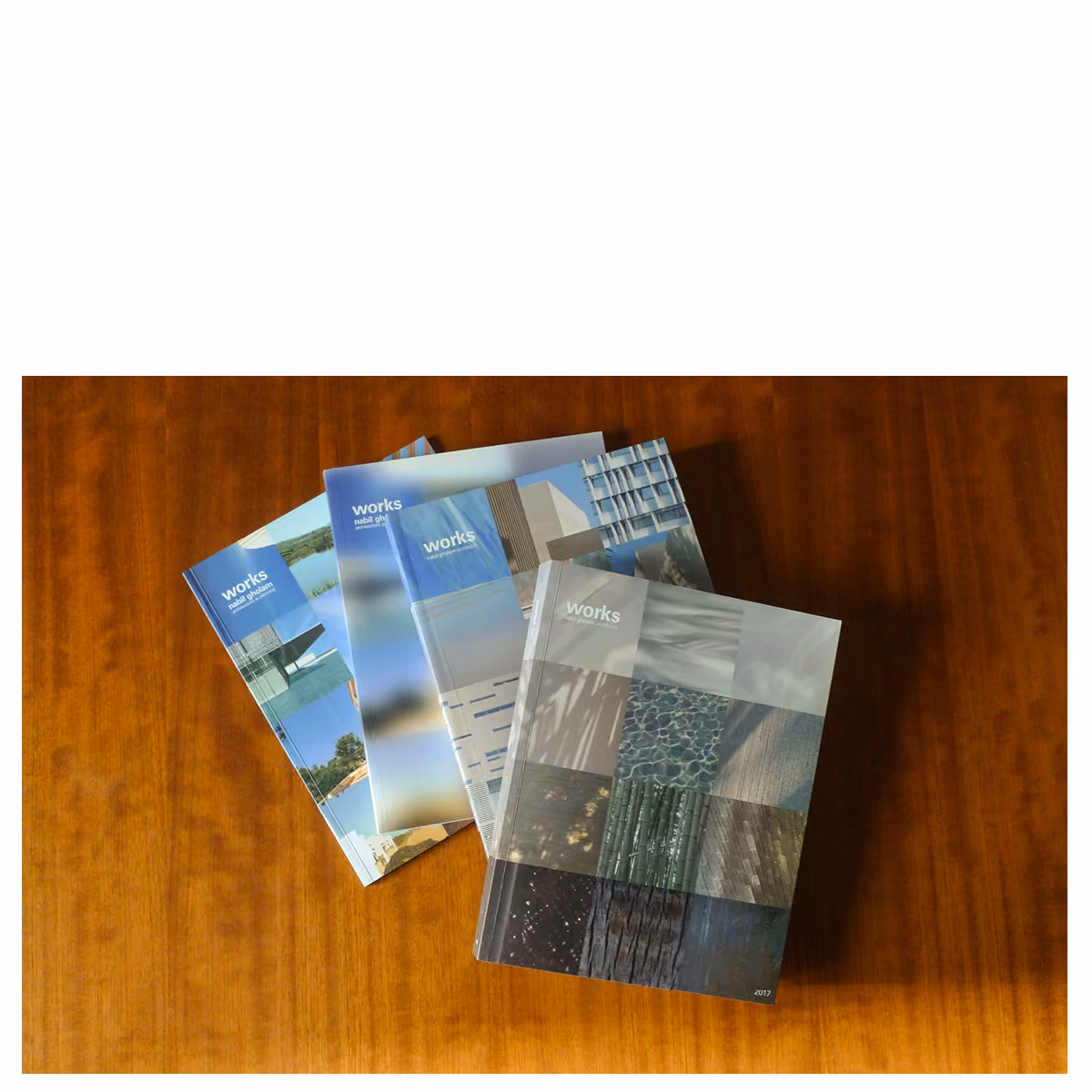 Four editions of the Works publication by Nabil Gholam Architects fanned out on a wooden table, with Works 2017 on top showing a photo-collage cover
