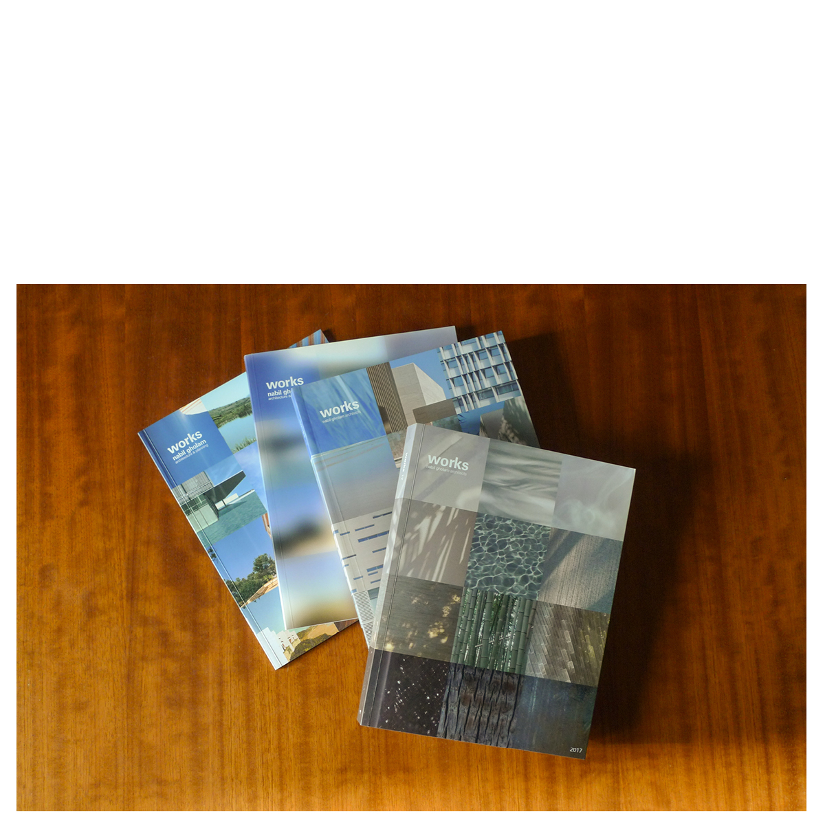 Four editions of the Works publication by Nabil Gholam Architects fanned out on a wooden table, with Works 2017 on top showing a photo-collage cover