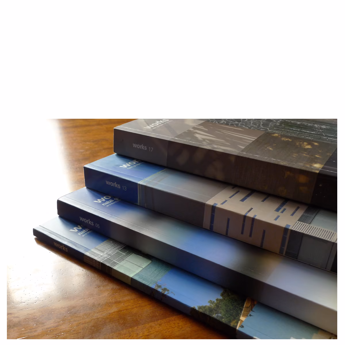 Stacked spines of Works 2017 and earlier Works editions by Nabil Gholam Architects, showing volumes 05, 13 and 17 fanned on a wooden table