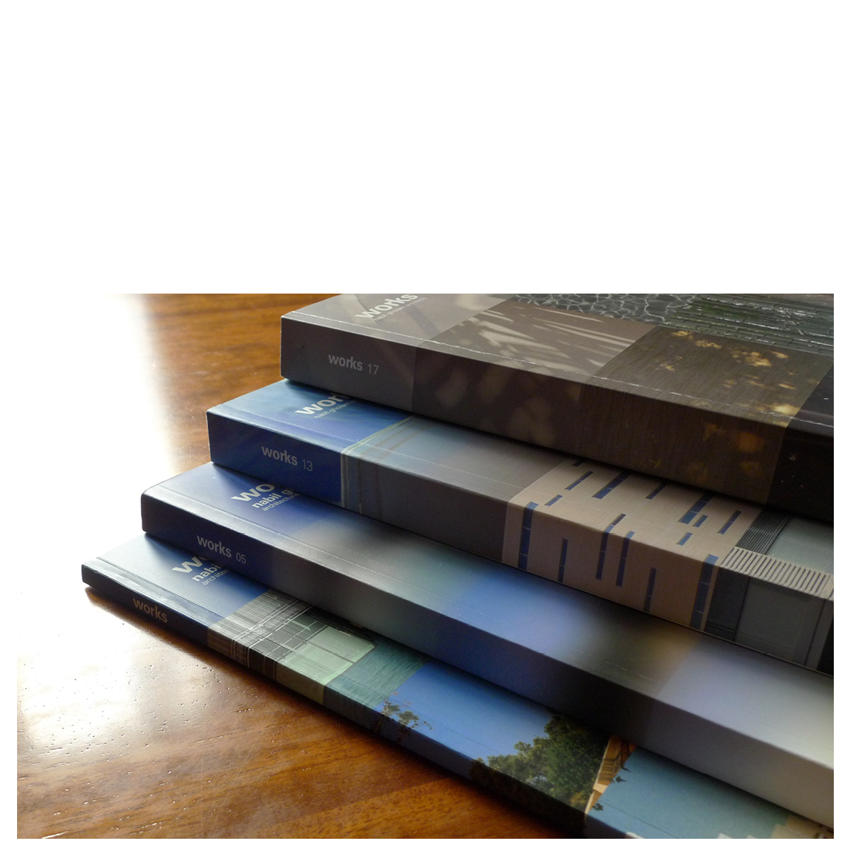 Stacked spines of Works 2017 and earlier Works editions by Nabil Gholam Architects, showing volumes 05, 13 and 17 fanned on a wooden table