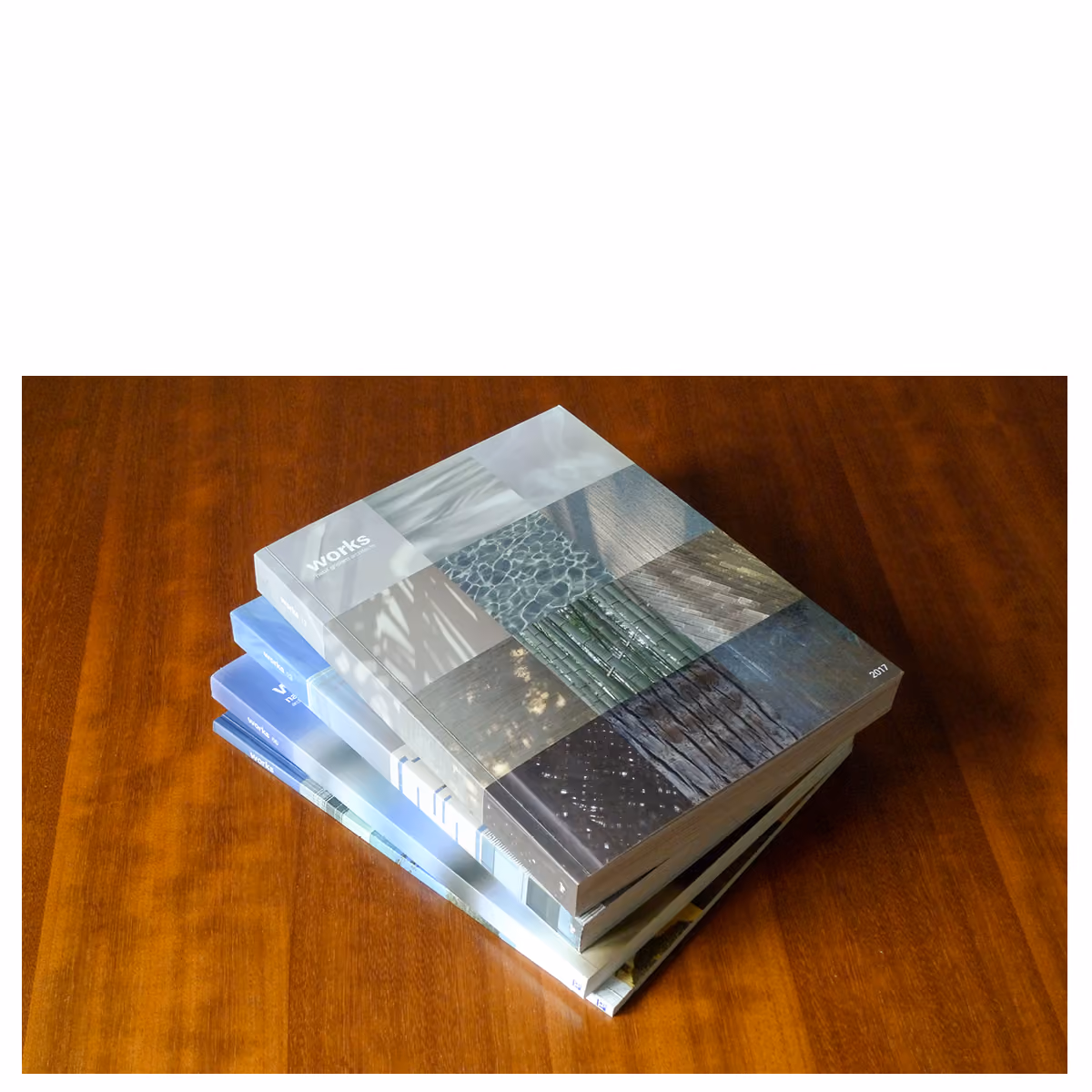 Stack of Works 2017 publication editions on a wooden table, the top cover showing a grid of textured material photographs