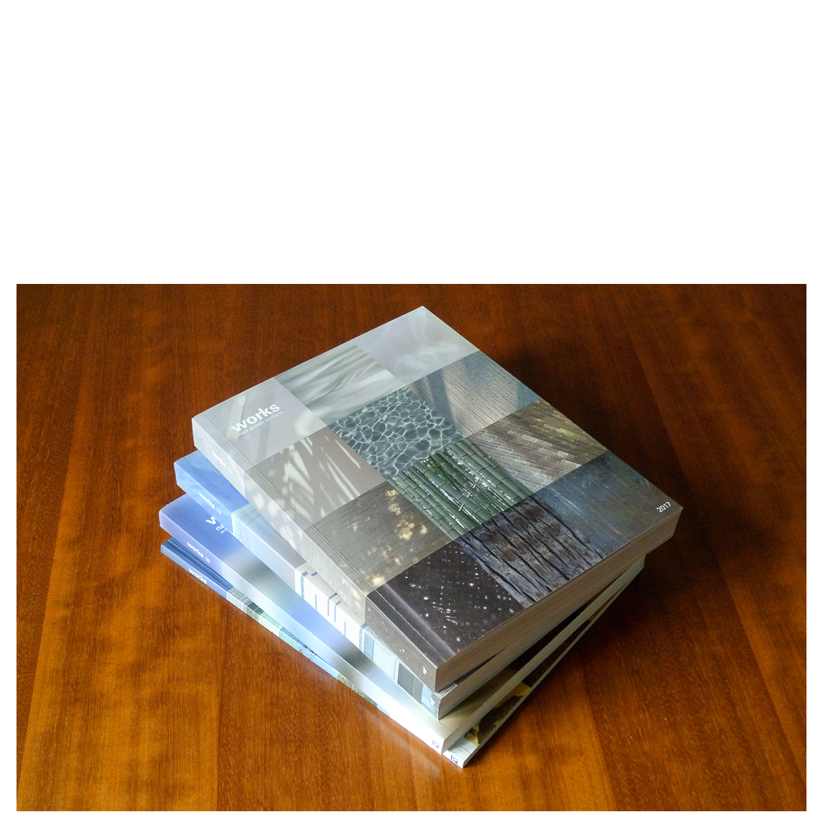 Stack of Works 2017 publication editions on a wooden table, the top cover showing a grid of textured material photographs