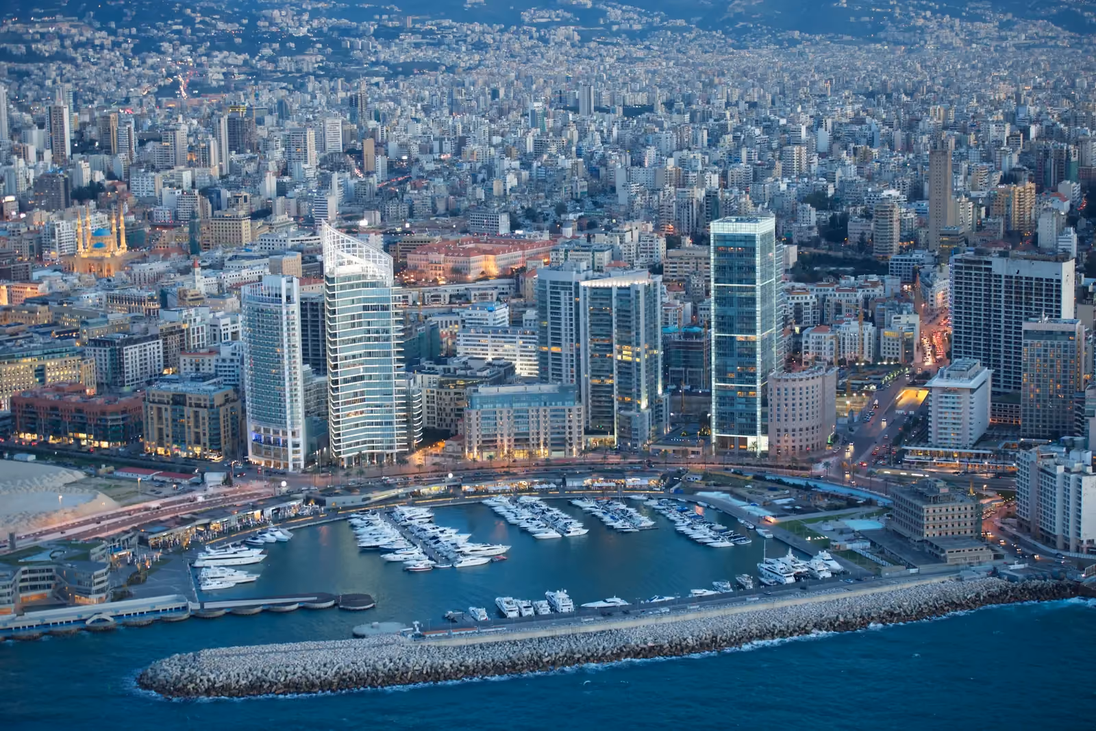 Aerial twilight view of Beirut Marina & Town Quay by Nabil Gholam Architects, a curved yacht harbour beside faceted glass towers within Beirut's dense skyline, Lebanon