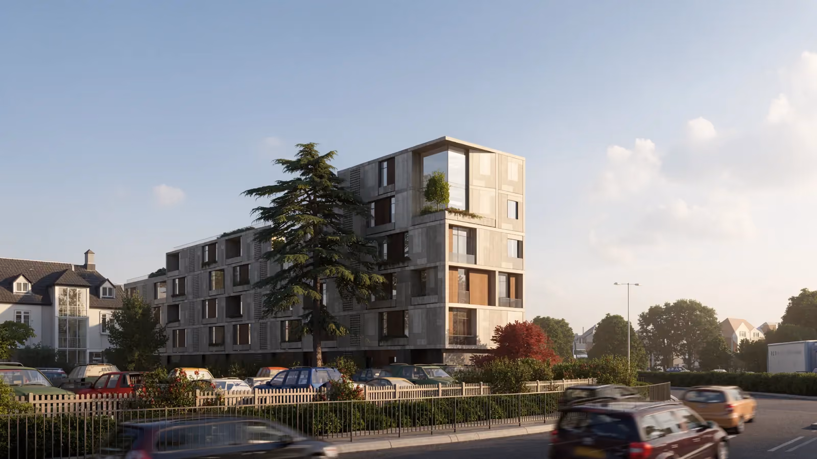 Parkway Road, a stone-clad residential building by Nabil Gholam Architects with staggered balconies and terraces, seen behind a mature cedar tree in Chelmsford, United Kingdom
