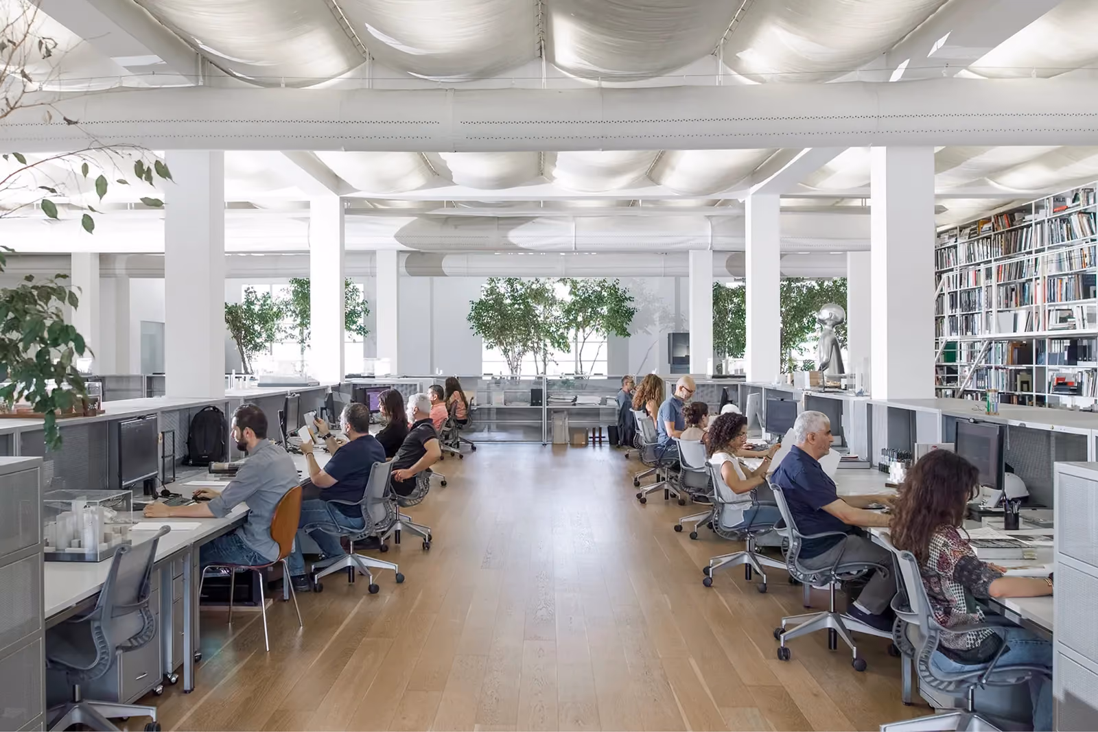 ngª Office in Beirut by Nabil Gholam Architects, an open-plan workspace with wooden flooring, staff at long desks, indoor plants and a draped fabric ceiling