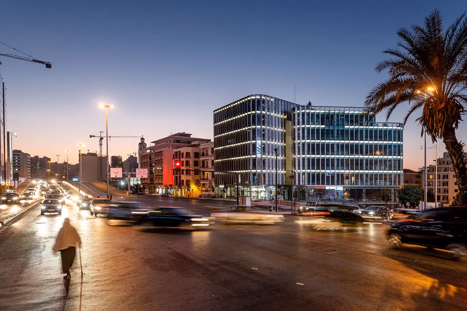 Saifi Plaza, a glass office building by Nabil Gholam Architects, illuminated at dusk on a busy Beirut junction with light-trailed traffic, Lebanon