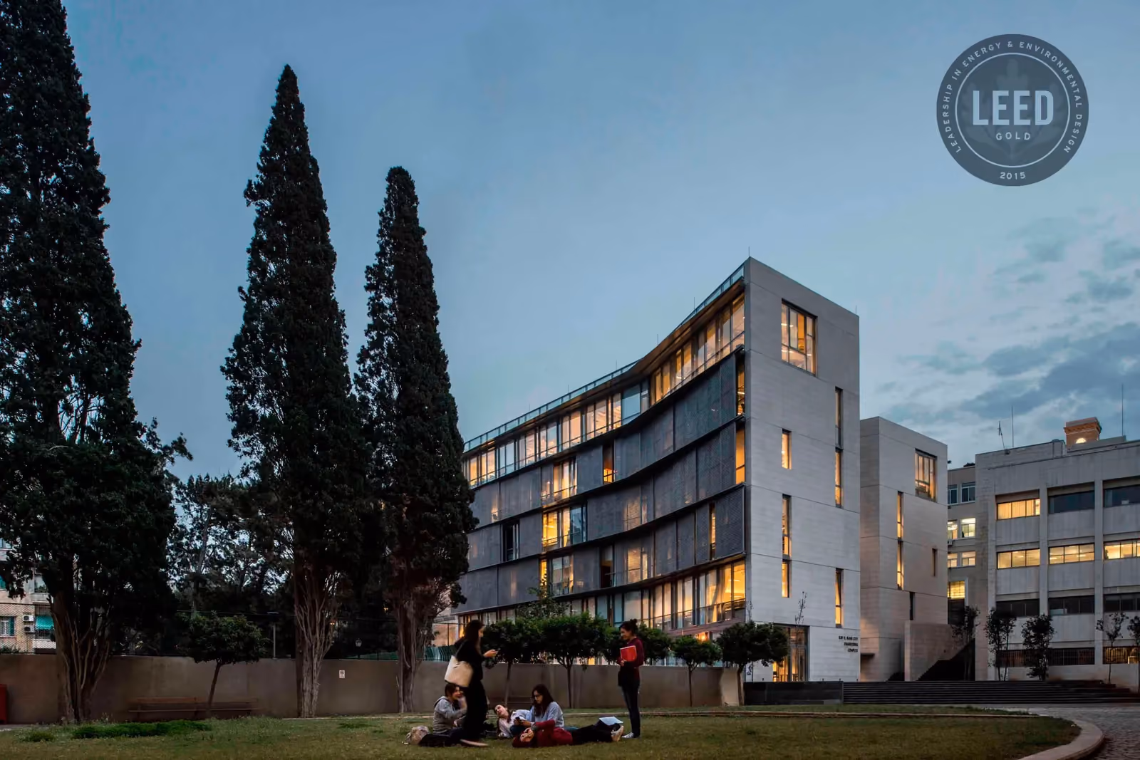 AUB IOEC Engineering Labs, a LEED Gold-certified building by Nabil Gholam Architects, illuminated at dusk with cypress trees and students on the lawn in Beirut, Lebanon