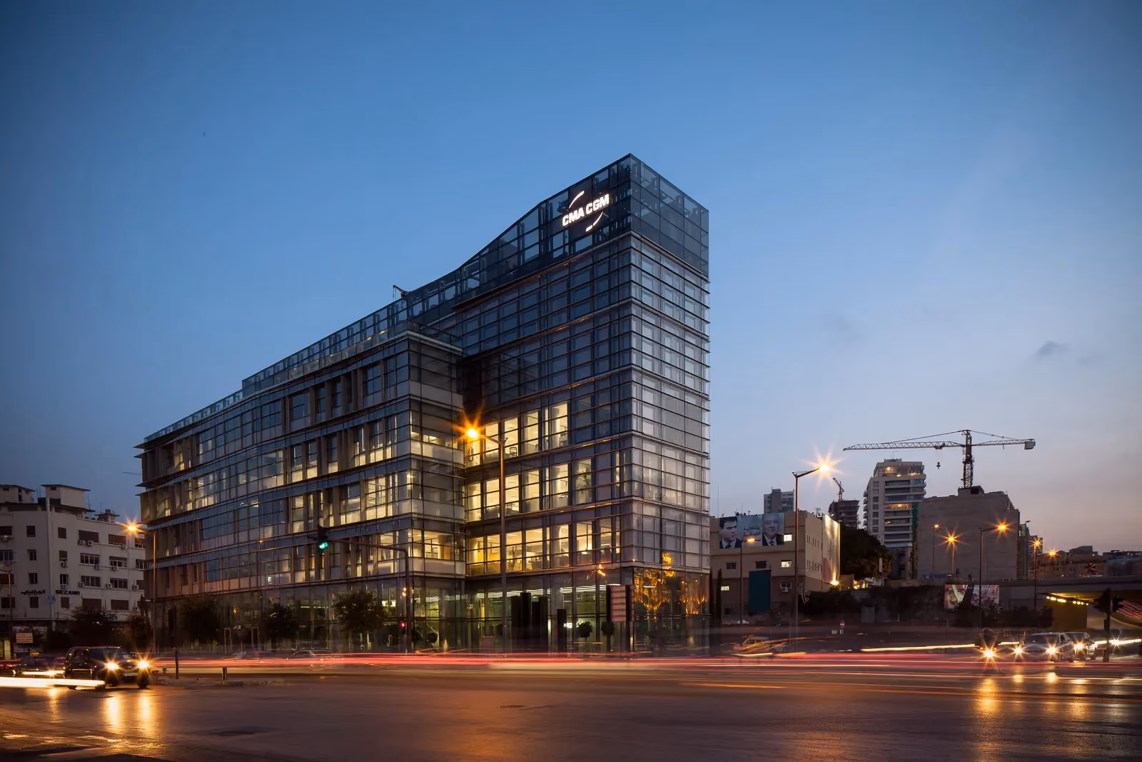 CMA-CGM Headquarters, a faceted glass office tower by Nabil Gholam Architects, illuminated at dusk above a busy Beirut street with light trails from traffic, Lebanon