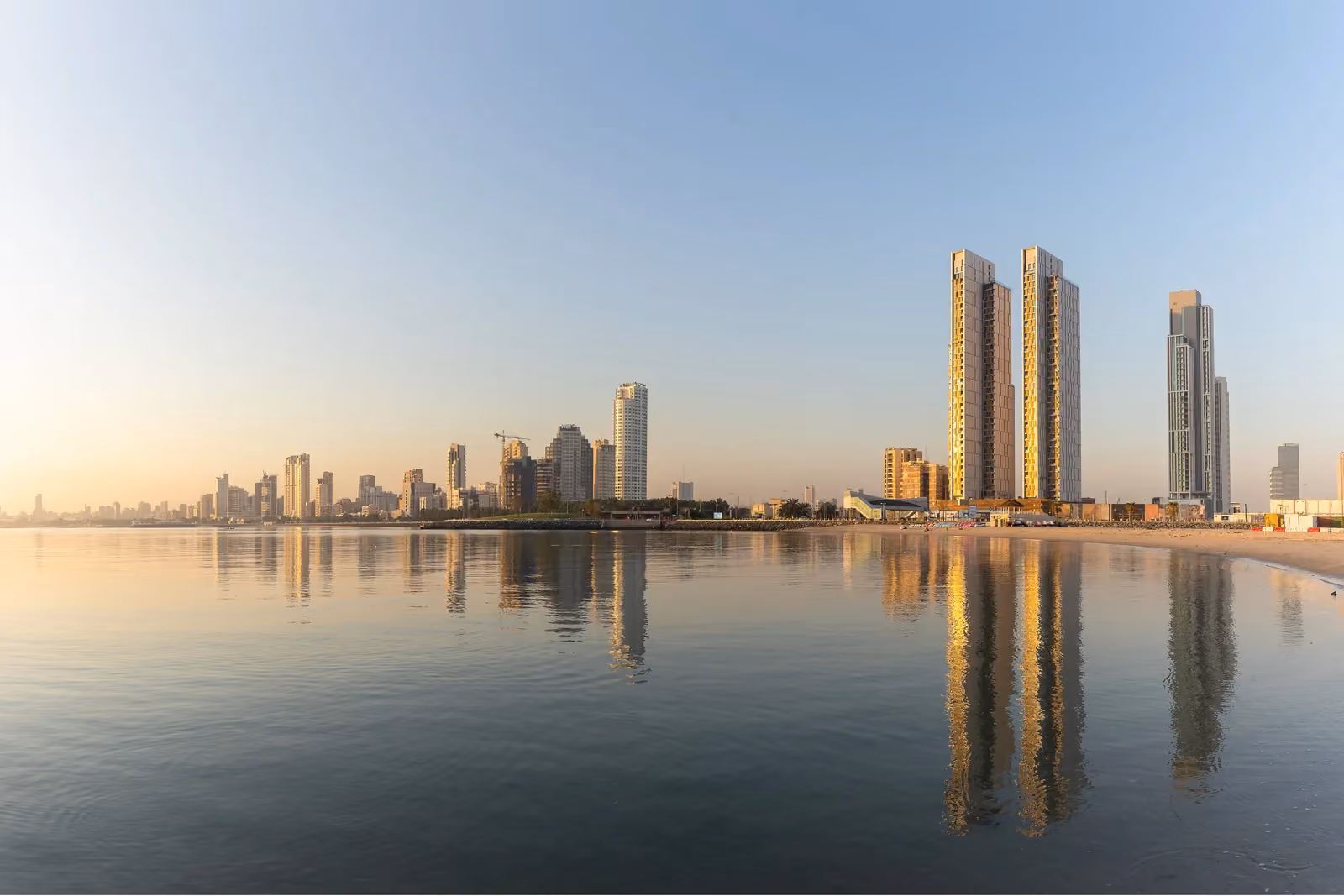 Hessah Al Mubarak twin high-rise towers by Nabil Gholam Architects, rising above the waterfront skyline of Kuwait City, Kuwait, reflected in calm sea at dusk