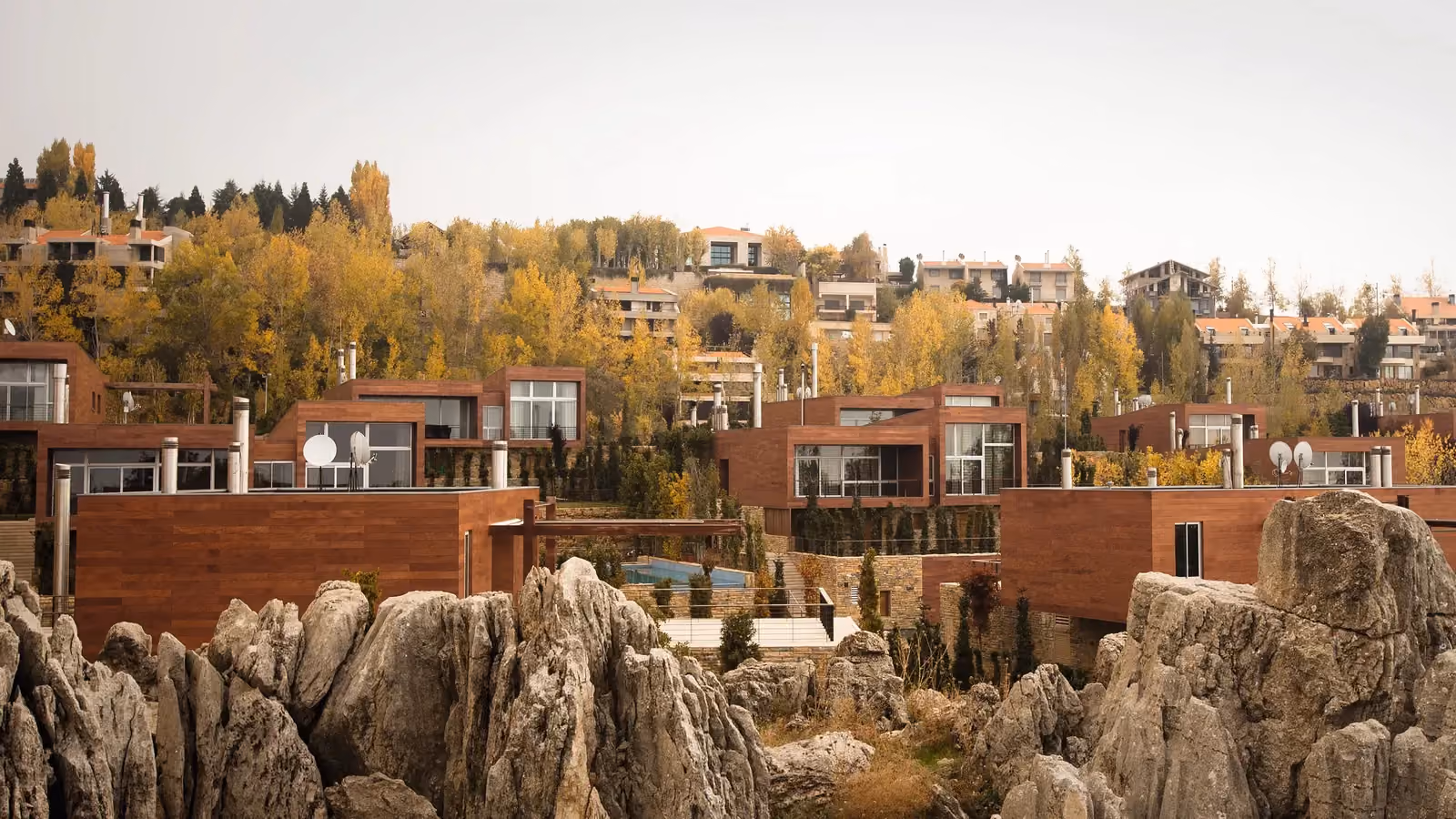 Clouds, a cluster of wood-clad villas by Nabil Gholam Architects, set among jagged limestone rock formations and autumn foliage in Faqra, Lebanon