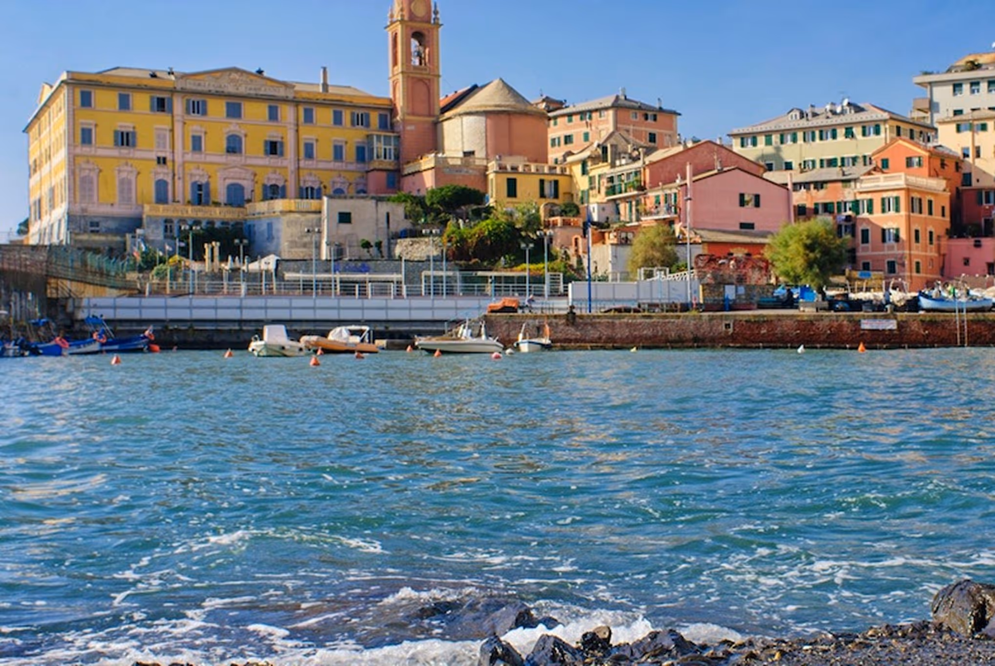 Вид на прибережне місто з кольоровими будинками, хвилями та човнами на воді.