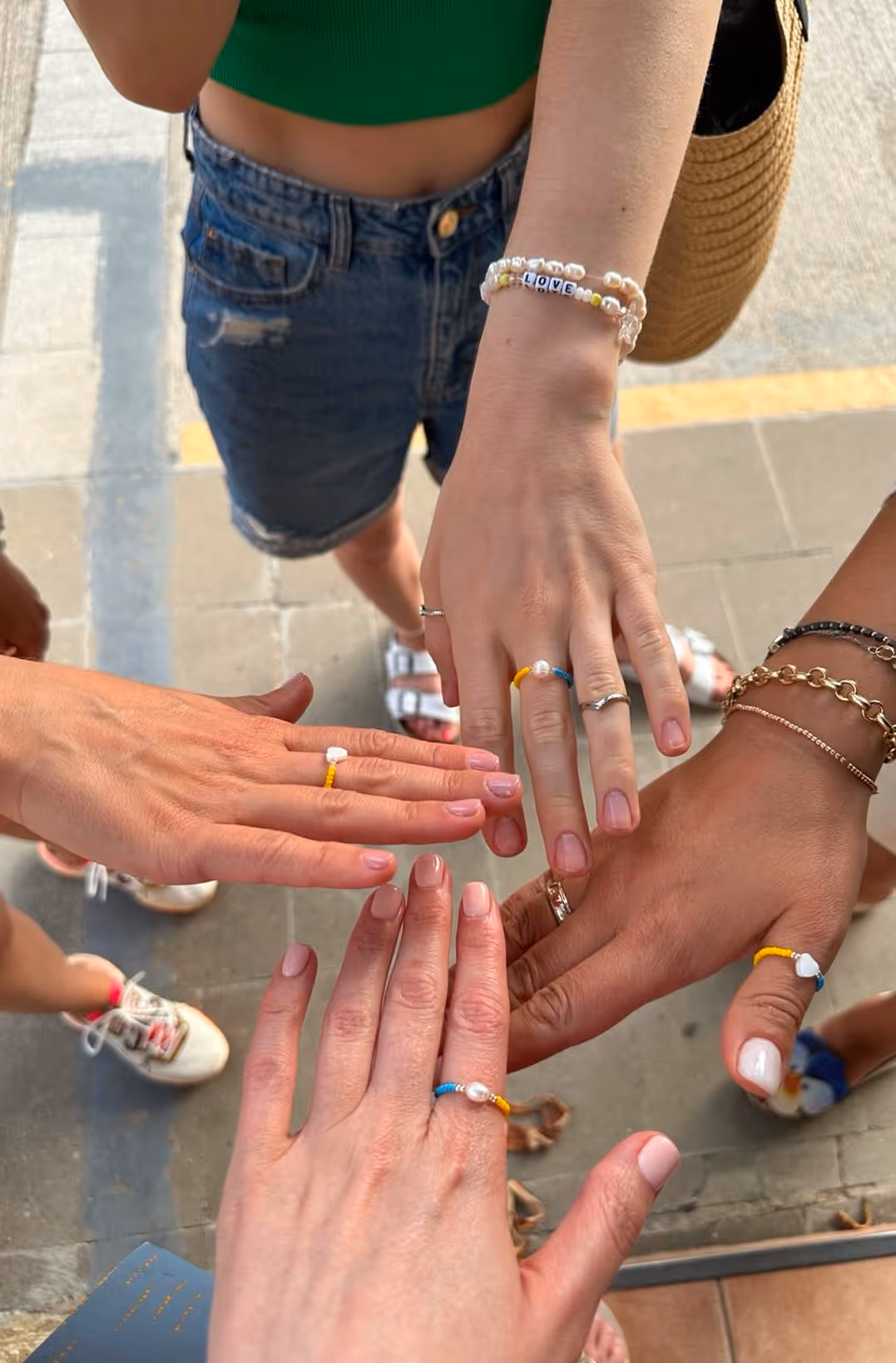 Чотири руки з різнокольоровими кільцями з бісеру та браслетом з написом LOVE над тротуаром — Enjoy 2026, Інтенсив MIGIS, інтенсив для гештальт-терапевтів
