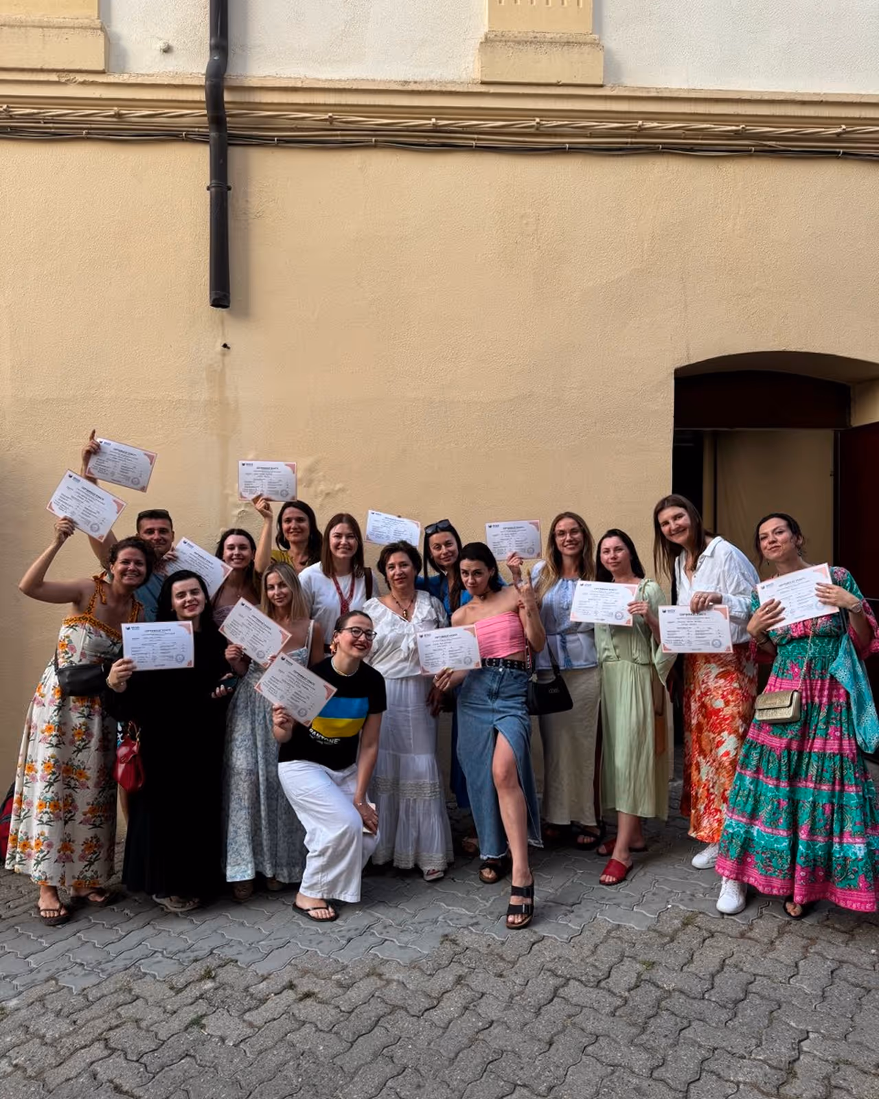 Група з 15 молодих людей із сертифікатами на тлі бежевої стіни у дворі. Enjoy 2026, Інтенсив MIGIS, інтенсив для гештальт-терапевтів