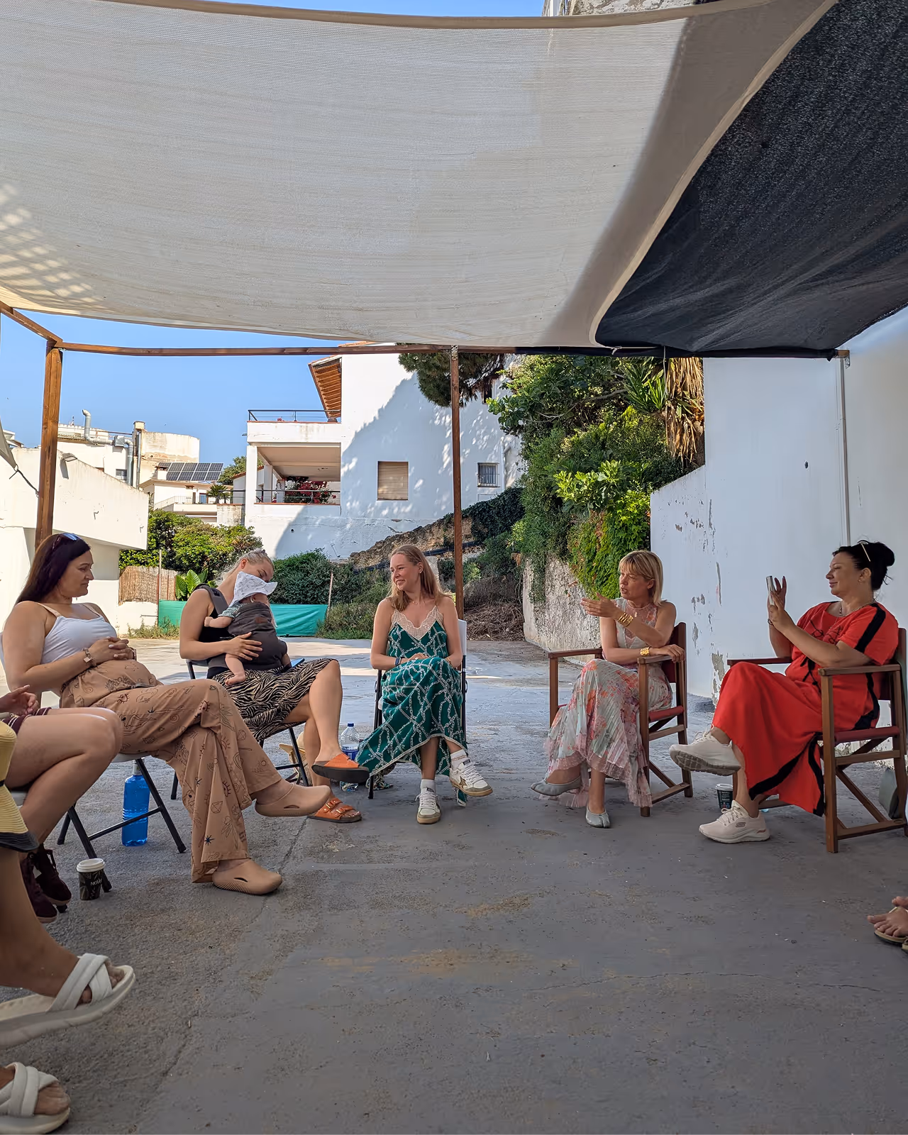 Група жінок сидить у колі на стільцях під навісом на вулиці, спілкуючись у сонячний день. Enjoy 2026, Інтенсив MIGIS, інтенсив для гештальт-терапевтів