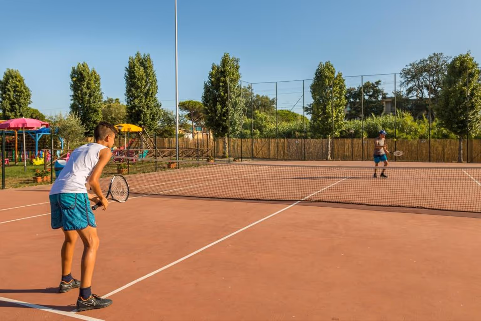 Двоє хлопців грають у теніс на відкритому корті в сонячний день. Villaggio Mare Si