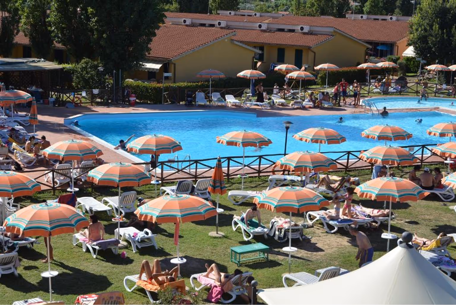 Відкритий басейн серед зелені з парасольками та людьми, що відпочивають на лежаках у сонячний день. Villaggio Mare Si