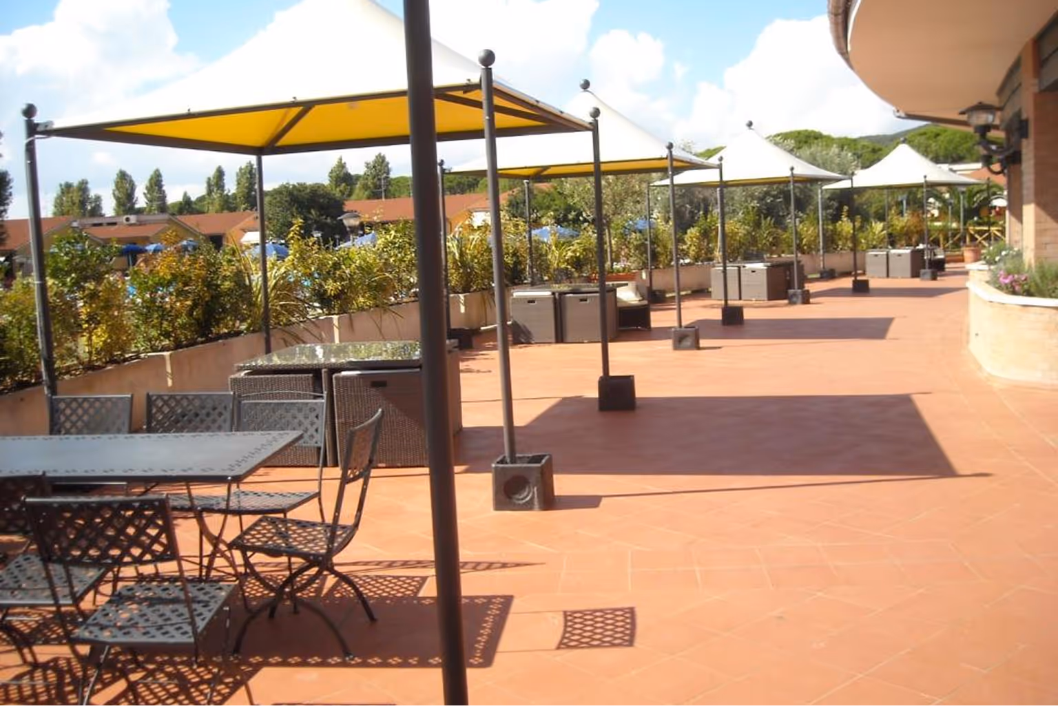 Тераса на відкритому повітрі з металевими столами і стільцями, накритими сонцезахисними навісами жовтого та білого кольорів. Villaggio Mare Si
