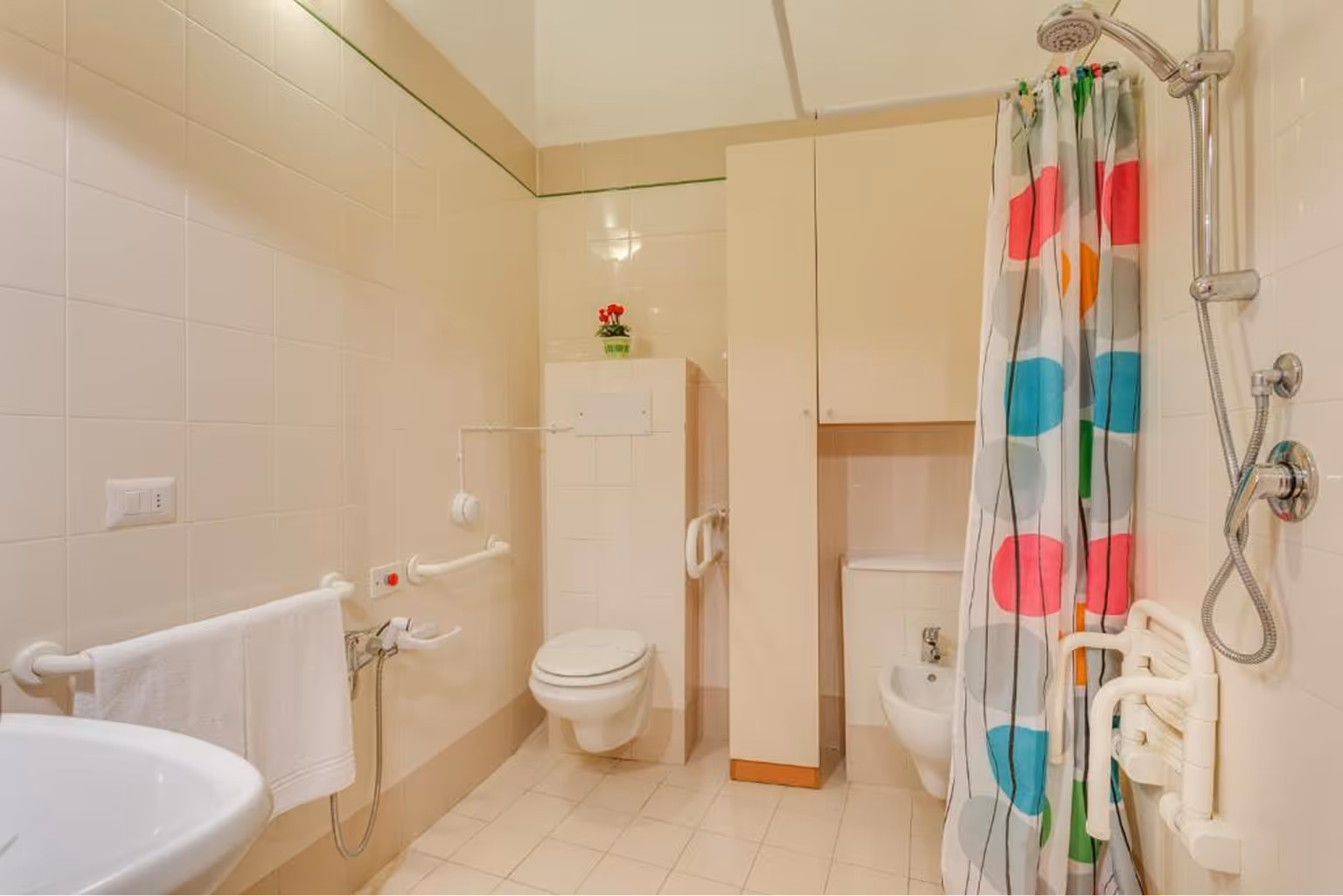 Ванна кімната з підвісним унітазом, умивальником, биде, душем із кольоровою шторкою та поручнями для безпеки. Villaggio Mare Si