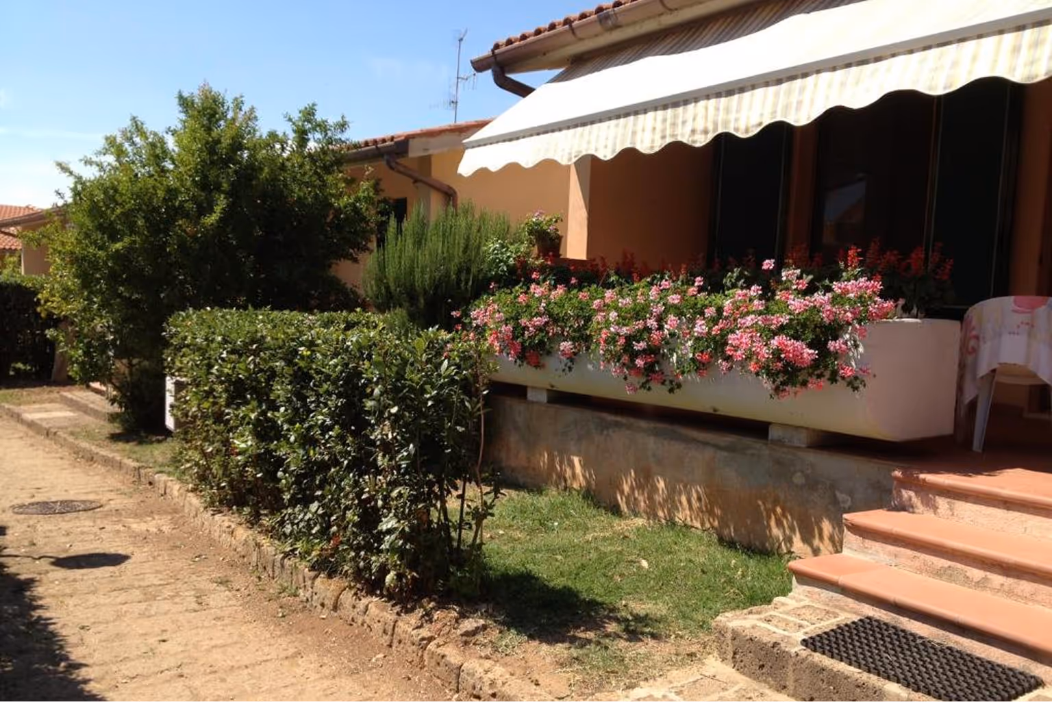 Будинок з терасою, обрамленою пишними рожевими квітами, з маркізою над вхідними дверима та зеленими кущами вздовж доріжки. Villaggio Mare Si