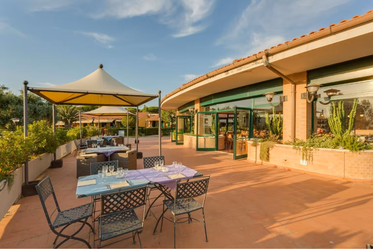 Затишна тераса ресторану з накритими столиками, металевими стільцями та зеленими рослинами під сонячним небом. Villaggio Mare Si