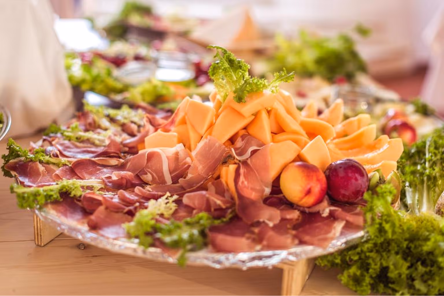 Плато з нарізаним прошутто, динею та фруктами, прикрашене зеленим листям салату. Villaggio Mare Si