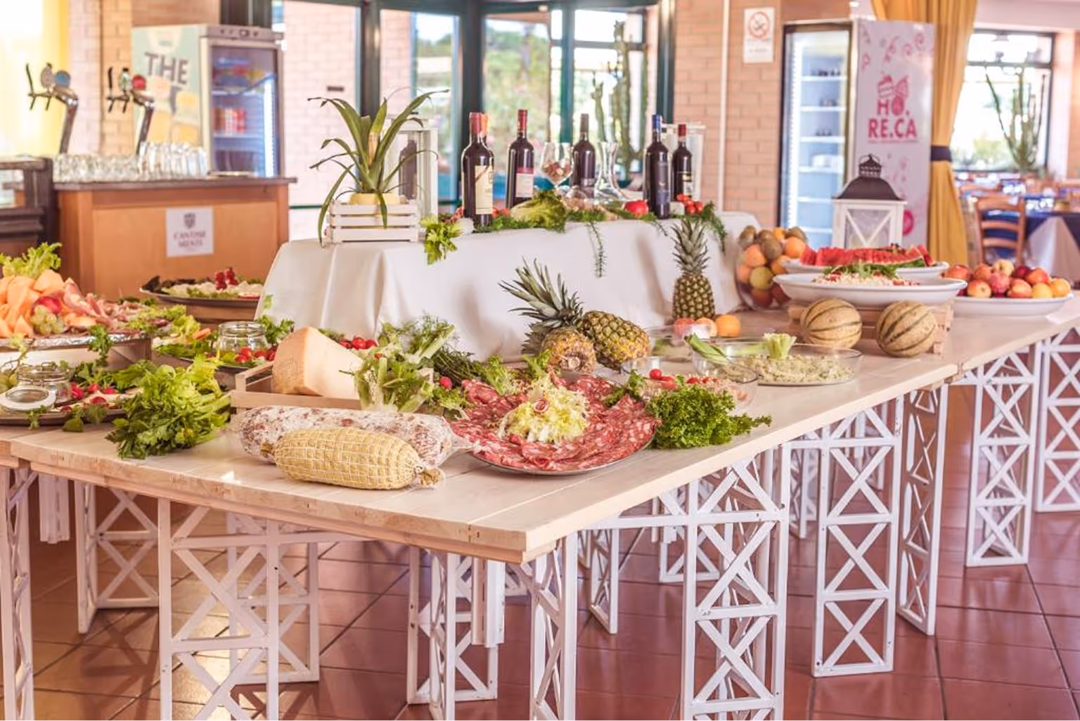 Стіл із різноманітними закусками та фруктами, включаючи ананаси, м'ясні делікатеси та пляшки вина в ресторані. Villaggio Mare Si