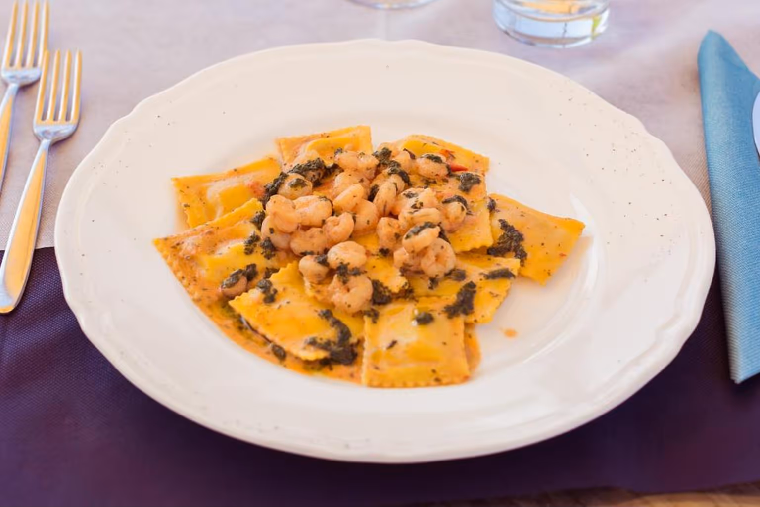 Тарілка равіолі з соусом та креветками, прикрашена дрібними чорними шматочками. Villaggio Mare Si