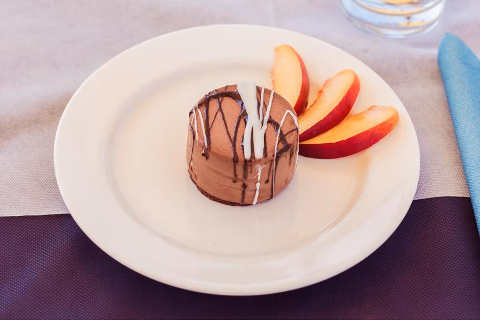 Шоколадний десерт з білою та темною шоколадною глазур'ю на білому блюді з трьома скибками нектарина. Villaggio Mare Si