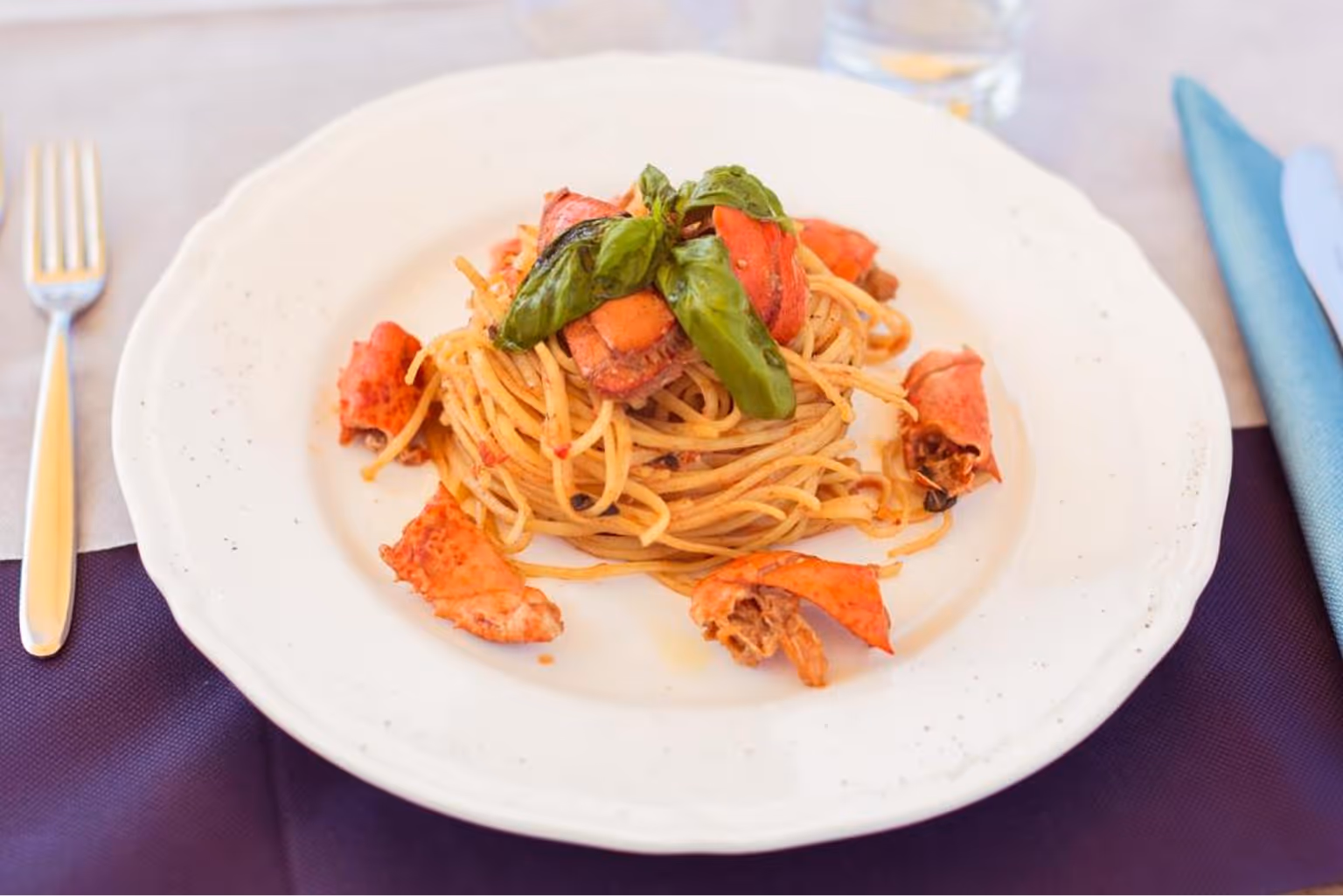 Паста спагеті з шматочками омара та зеленими листками базиліка на білій тарілці. Villaggio Mare Si