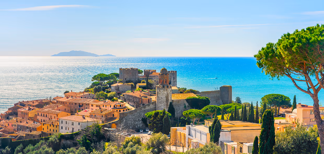 Вид на прибережне місто з середньовічним замком, помаранчевими дахами будинків та бірюзовим морем на тлі. Castiglione della Pescaia