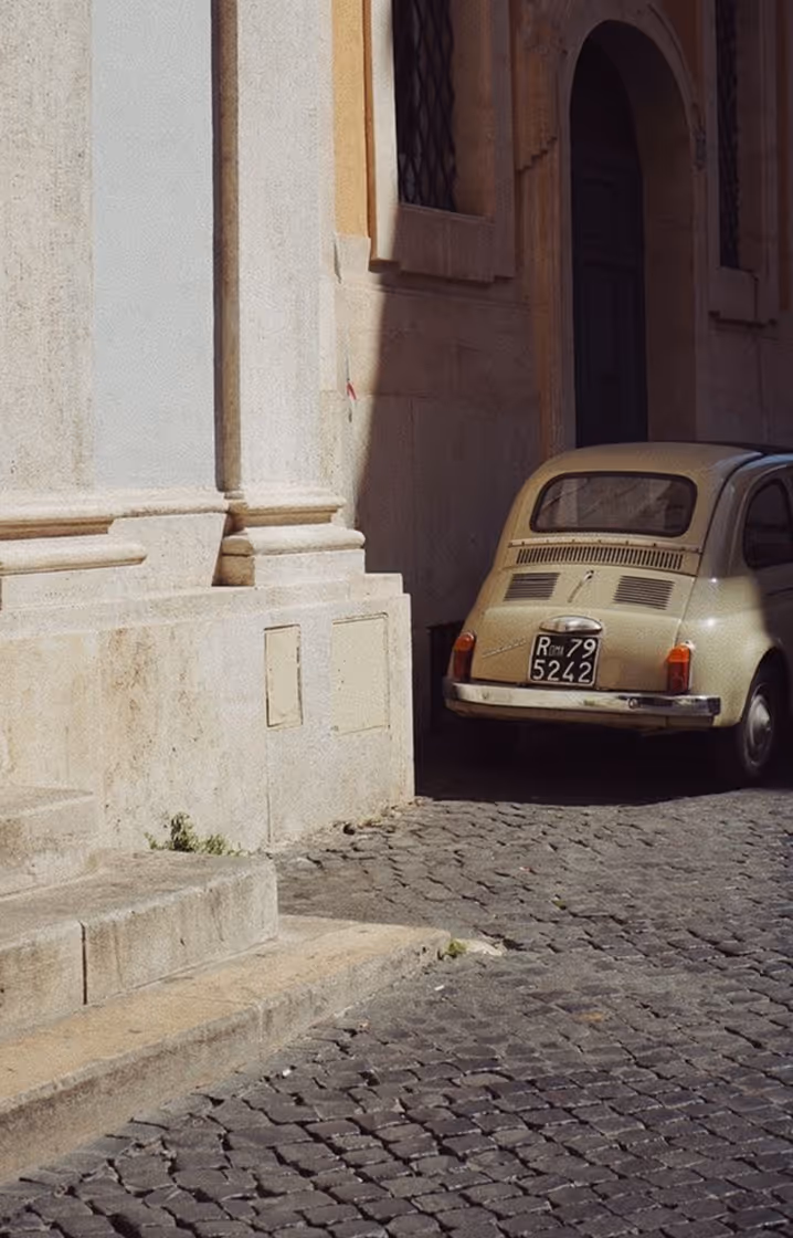 Старий бежевий автомобіль припаркований біля кам'яної будівлі на брукованій вулиці. Follonica, Toscana