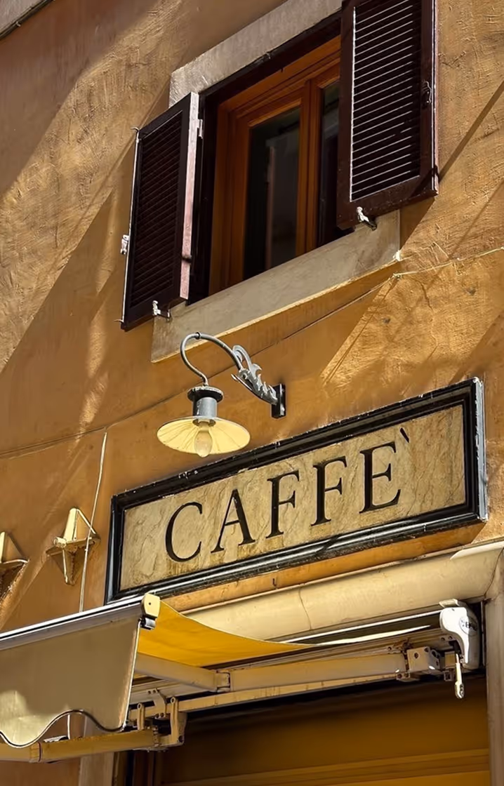 Вивіска з написом CAFFÈ на стіні жовтої будівлі під відкритим вікном з коричневими ставнями. Follonica, Toscana