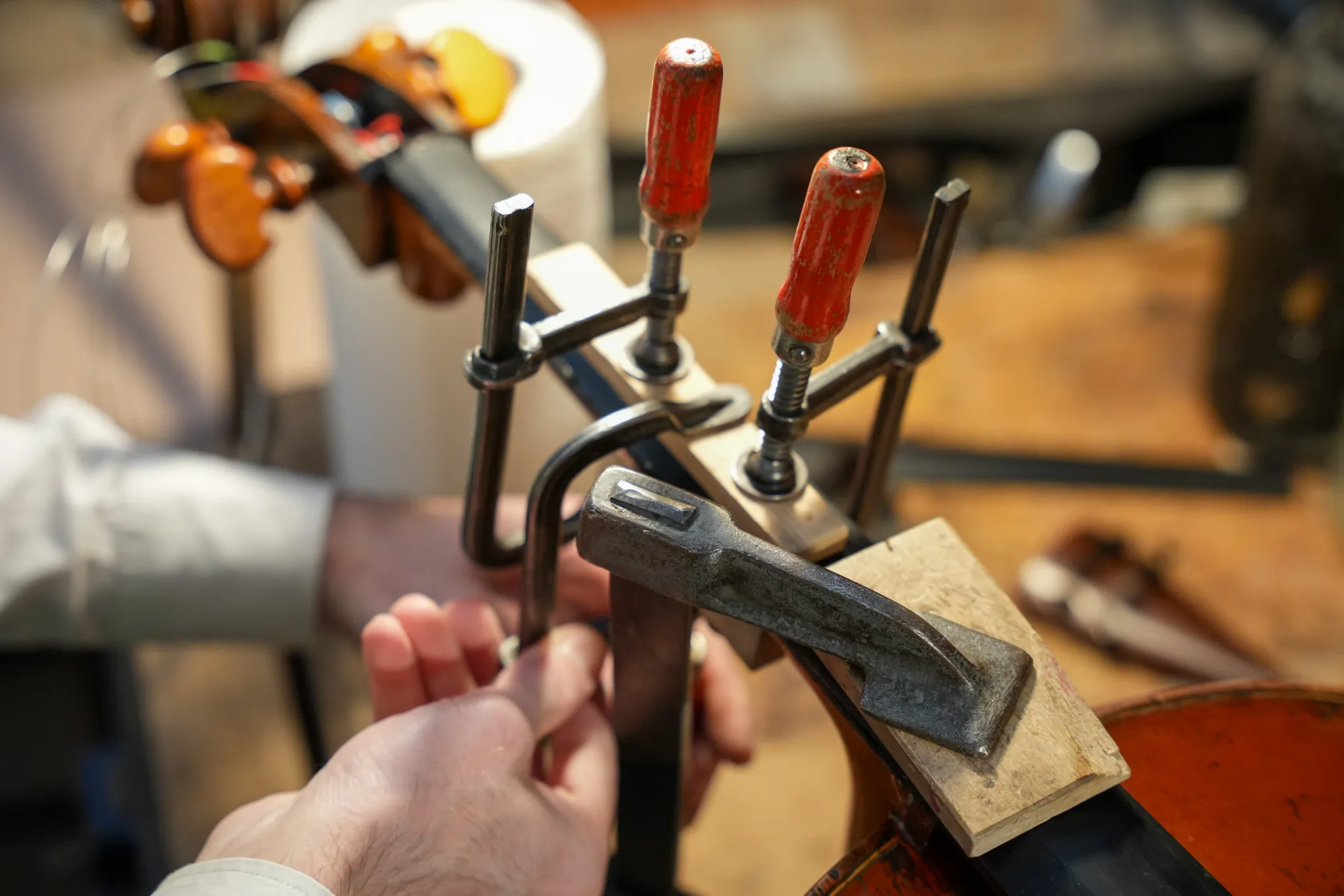 Mains serrant des pinces sur le manche d'un violon en réparation sur un établi en bois.