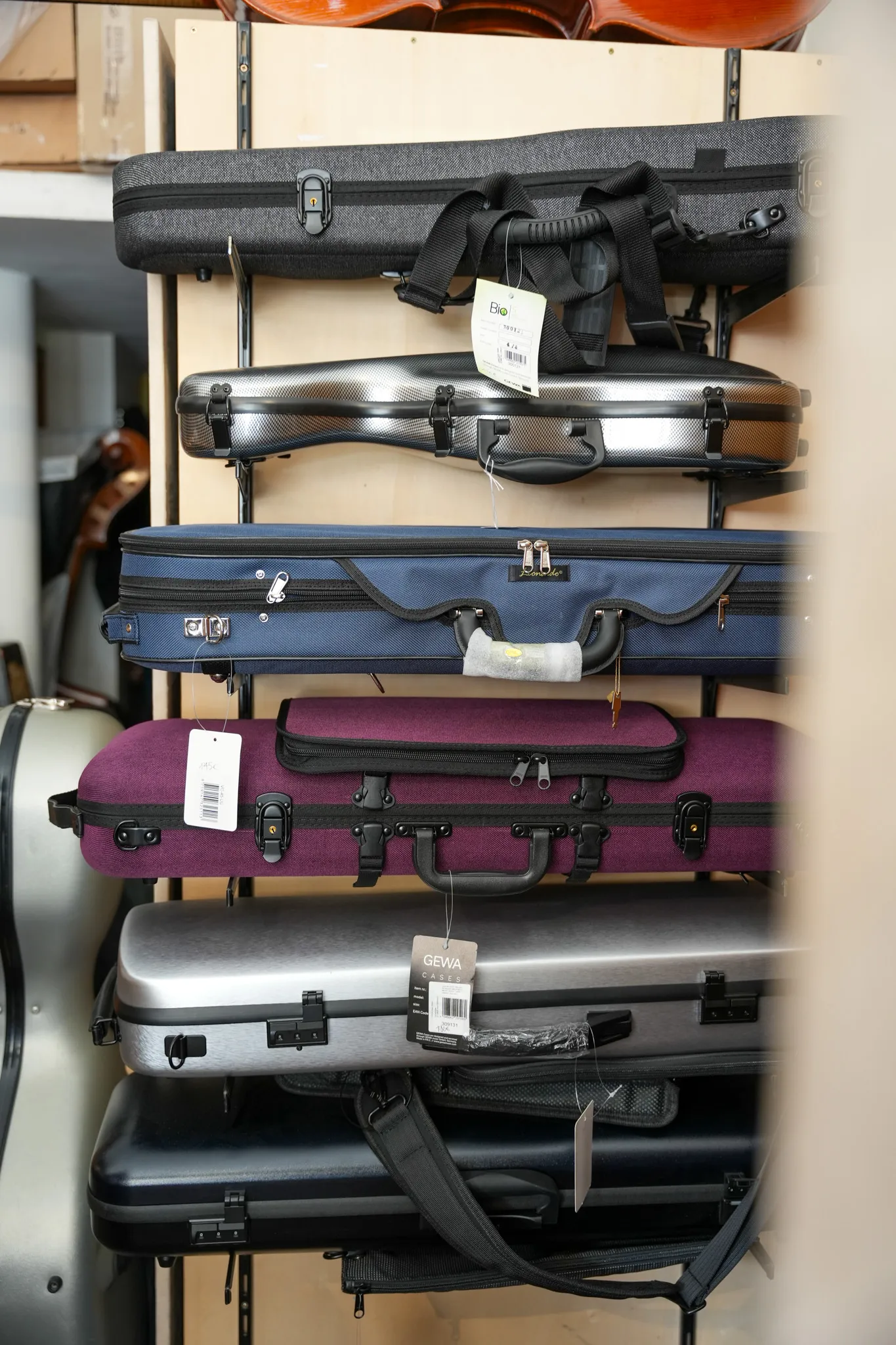 Cinq étuis rigides de différentes couleurs empilés sur une étagère, utilisés pour transporter des instruments de musique à cordes.
