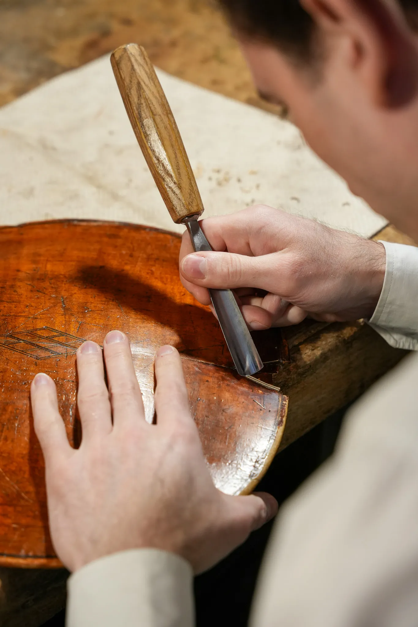 Une personne répare ou sculpte la caisse en bois d'un violon avec un ciseau à bois.